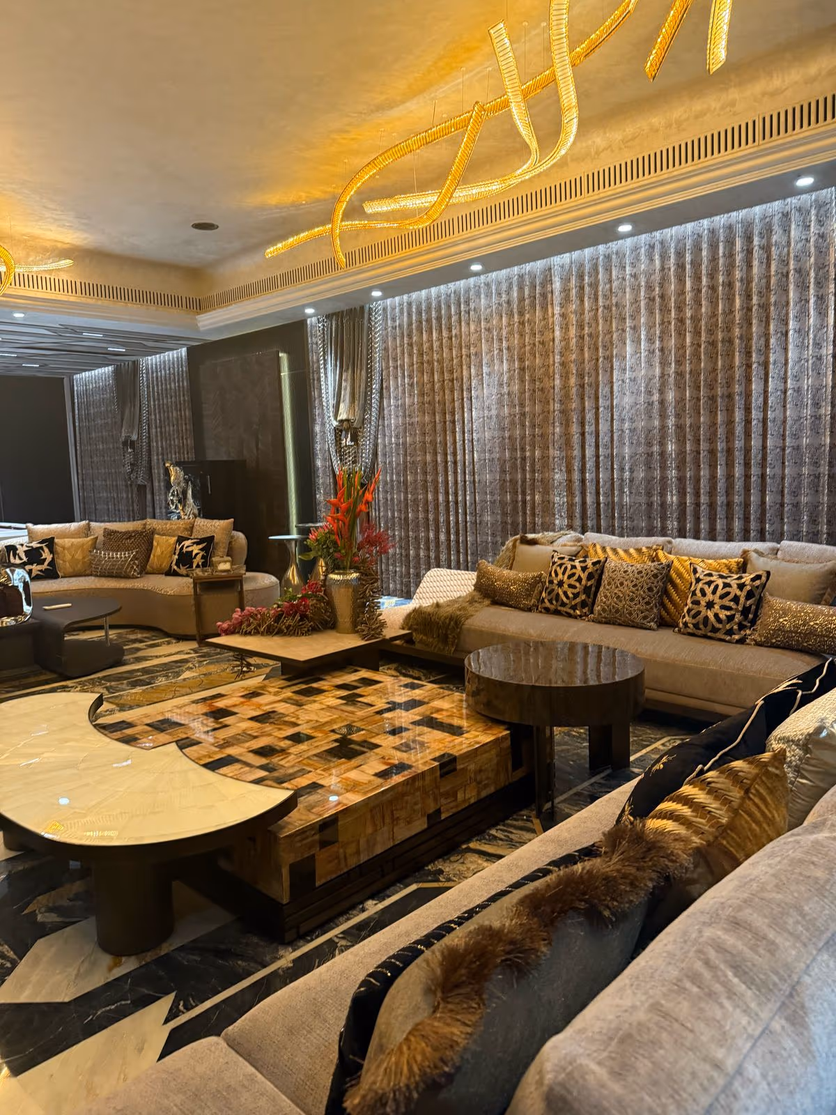A Designatore living room furnished end to end — curved velvet sofas, an agate coffee table and a gold ribbon chandelier.