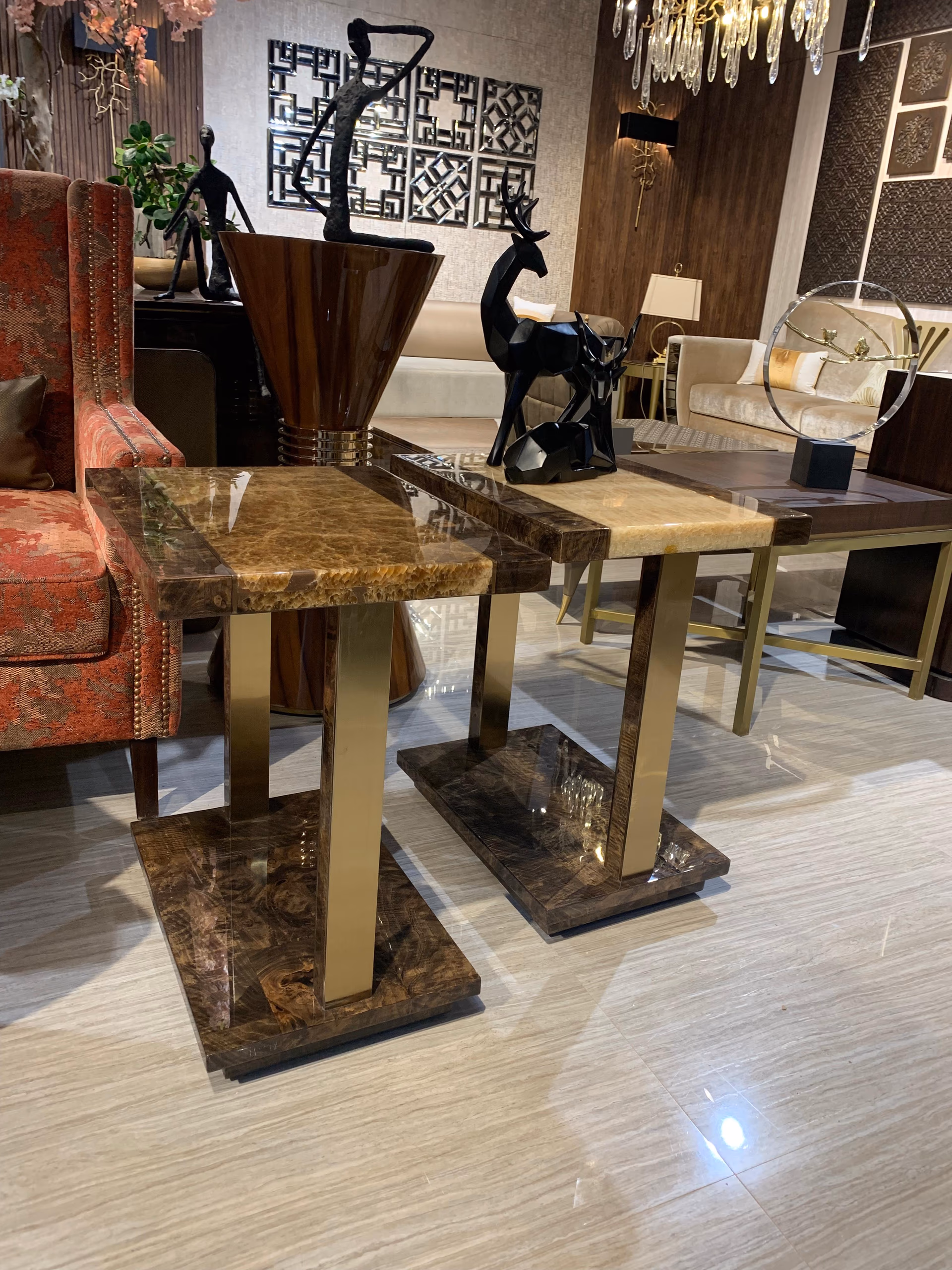Pair of C-shaped side tables in glossy burl wood with glowing amber onyx tops and slim brass column supports, set together on a light floor.
