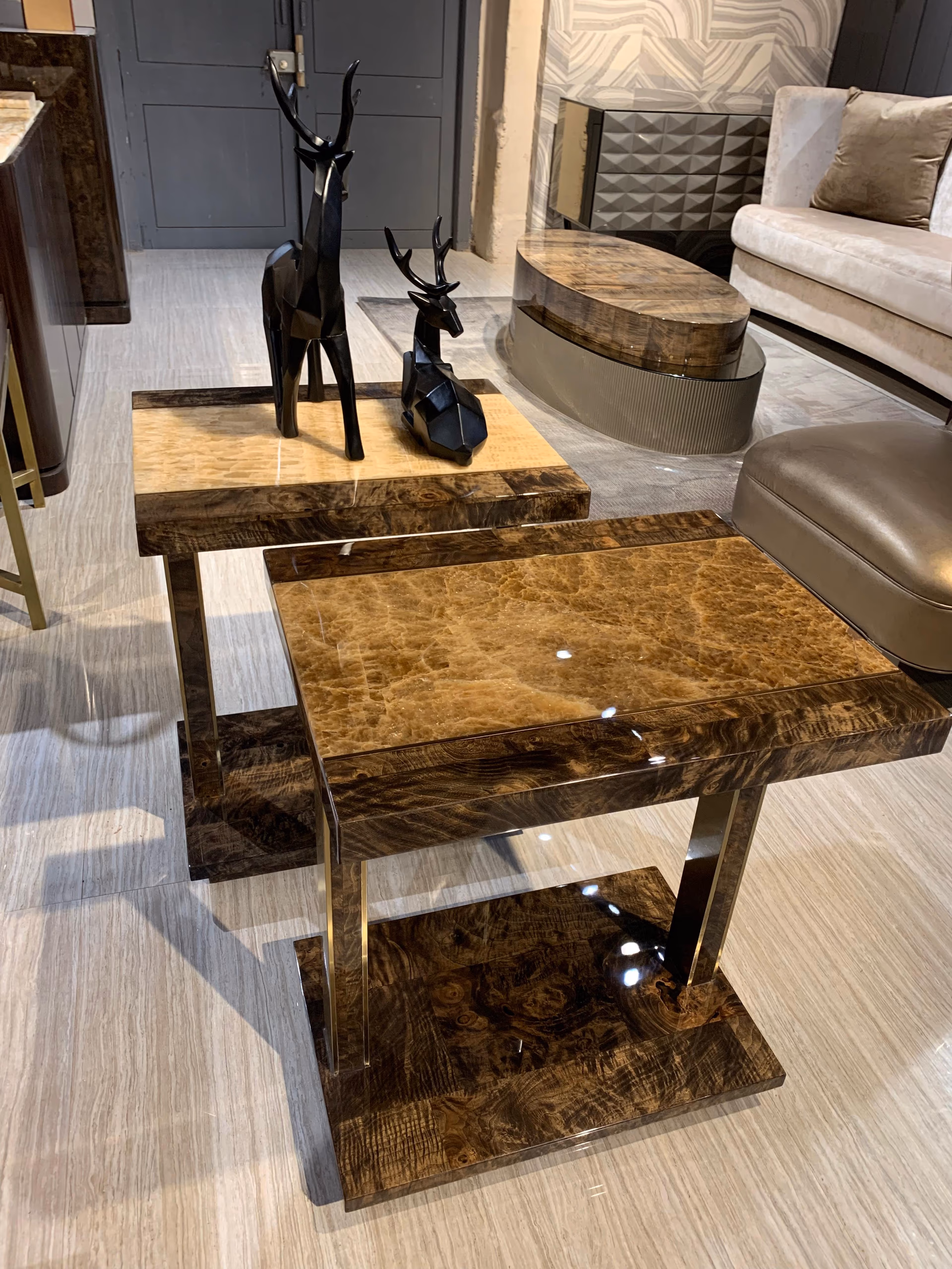 Closer angled view of the amber onyx and burl-wood side tables, showing the warm veining in the stone tops and the brass detail on the supports.