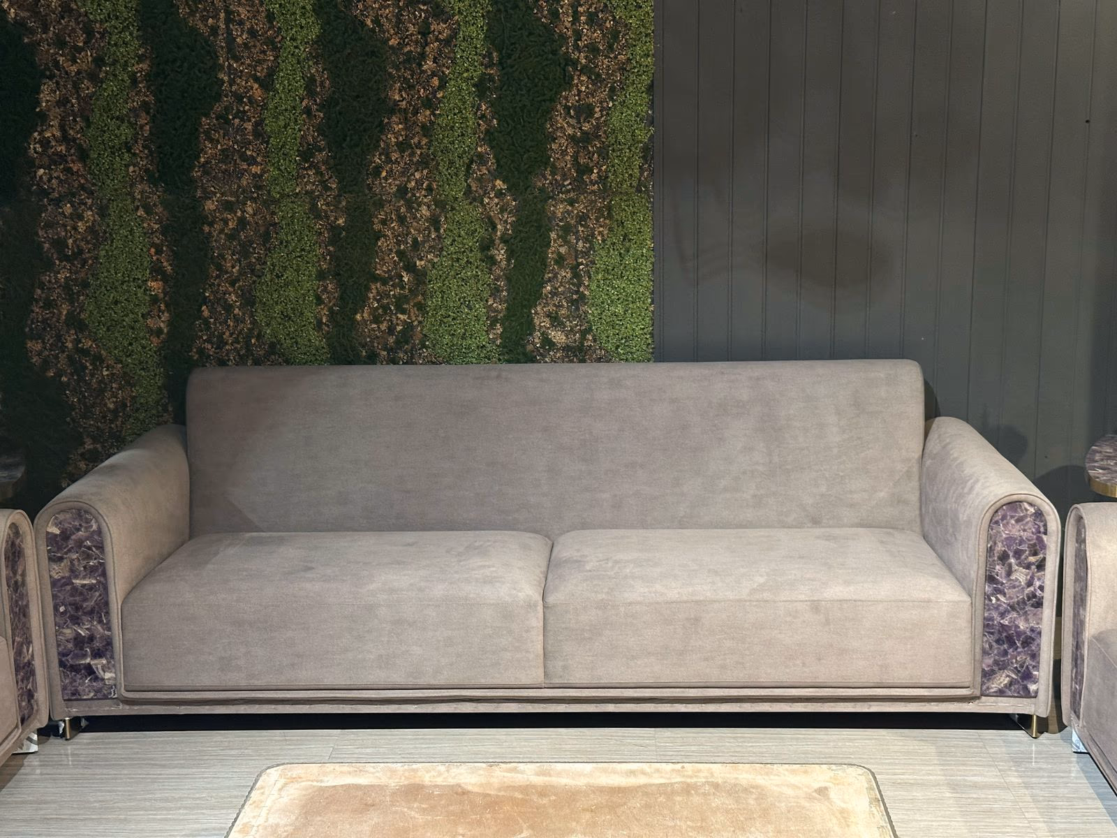 Grey velvet sofa with raw amethyst crystal side panels set in brass trim against a living moss wall.