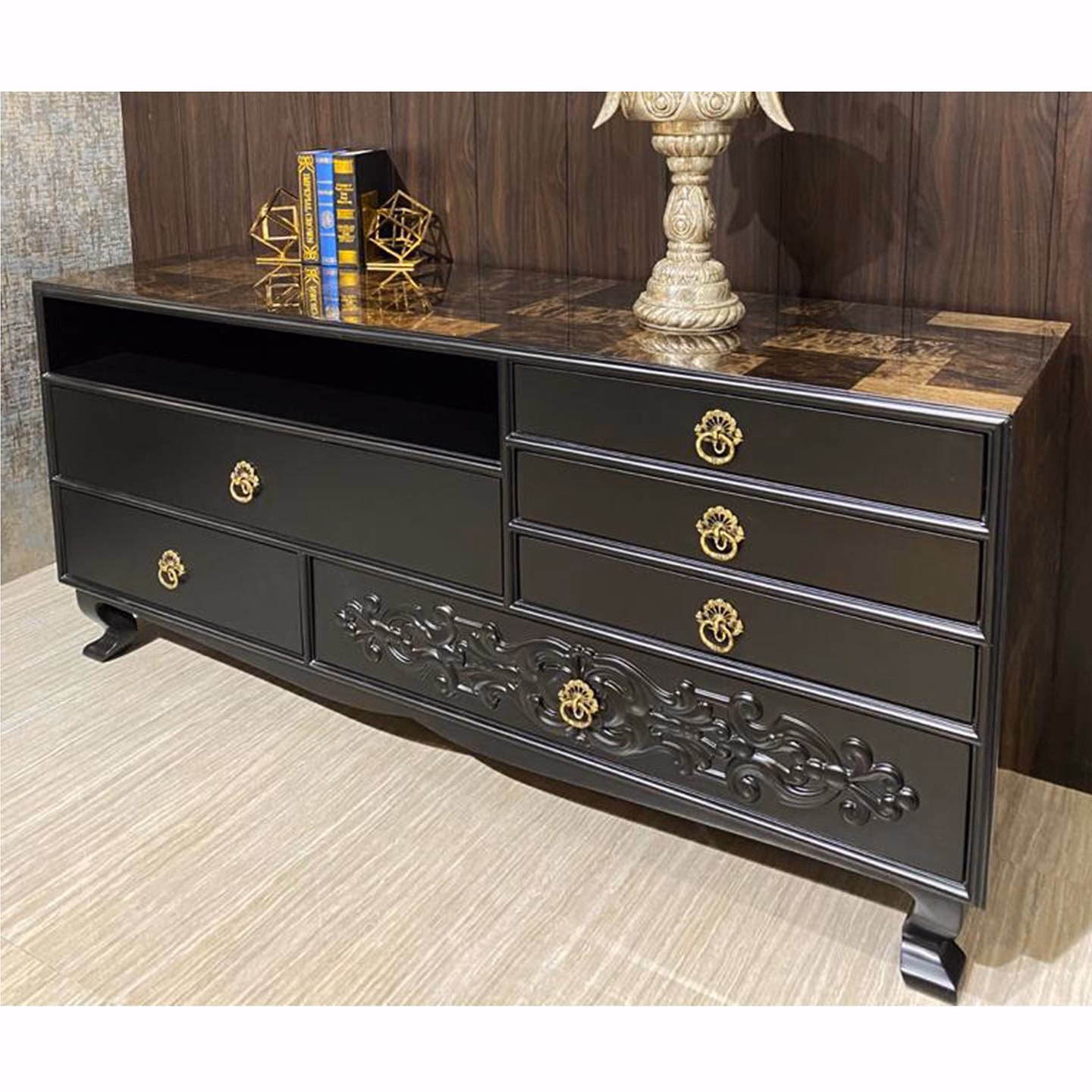 Straight-on view of the black carved sideboard showing the full run of drawers, the scrolled centre carving and the burl top against dark walnut panelling.
