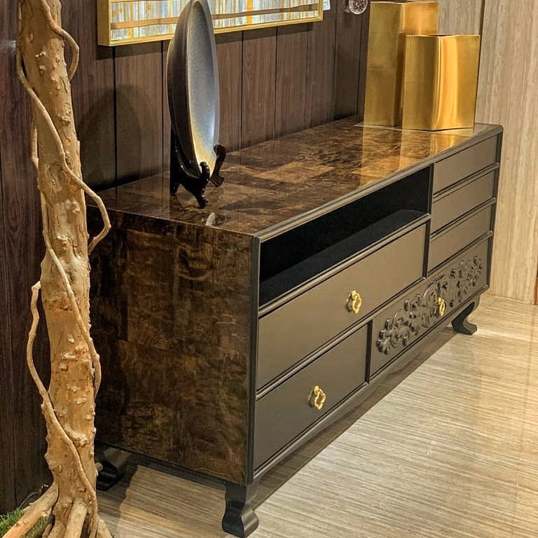 Long black lacquer sideboard with a hand-carved scrollwork drawer front, antique-gold clover pulls, an open media shelf and a polished burl-wood top, standing on carved cabriole feet.