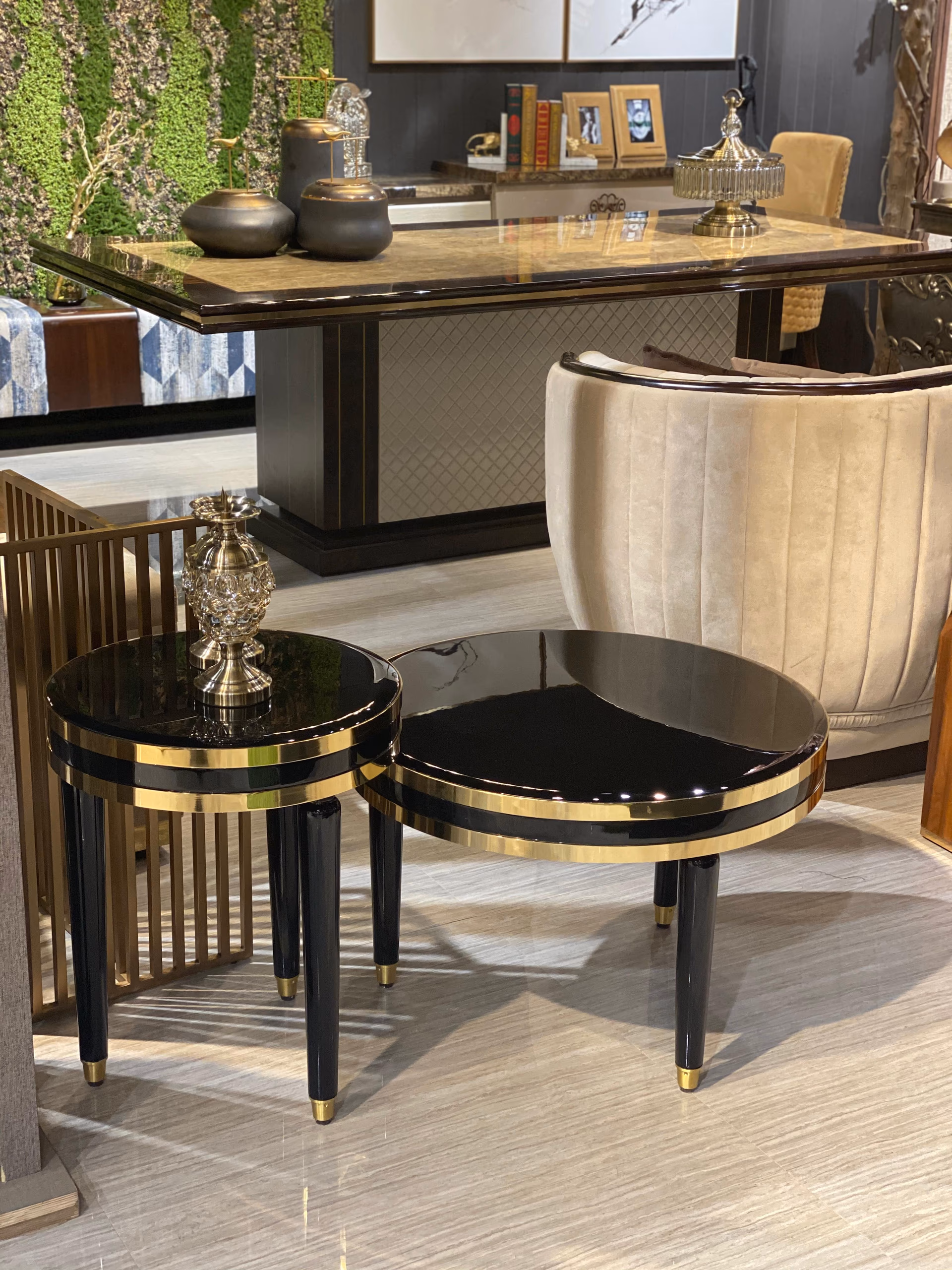 Two round side tables with high-gloss black tops ringed by thin gold bands, standing on splayed black tapered legs with brass feet on a pale floor.