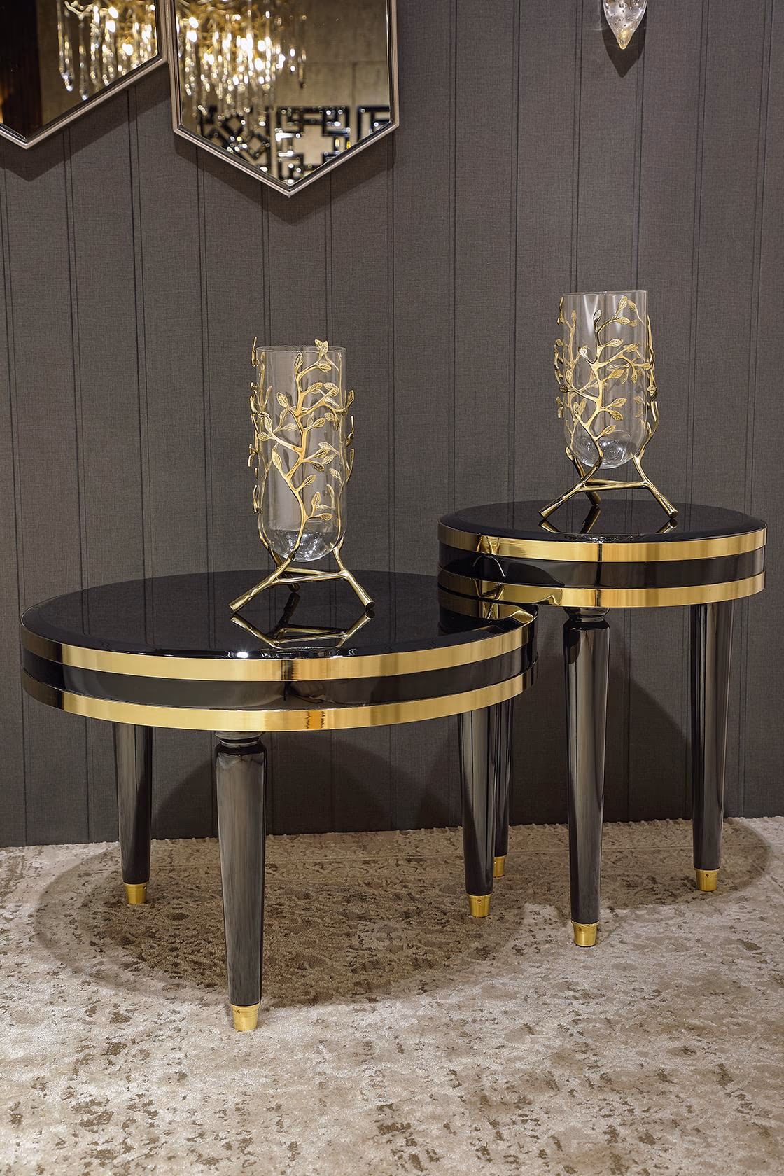 Pair of round side tables at two heights with glossy black tops, polished gold band trims and tapered black legs with gold caps, styled with gold-leaf vases.