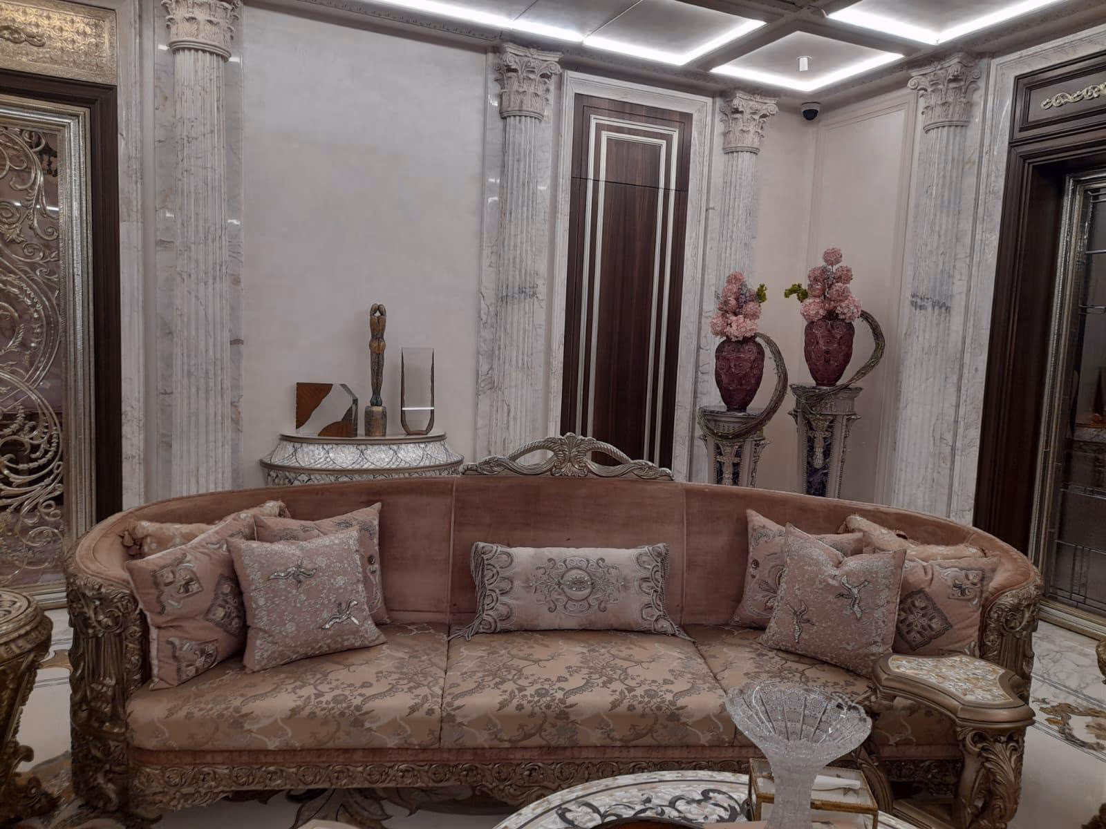 Blush carved curved sofa with a gilt frame and patterned cushions in a classical living room