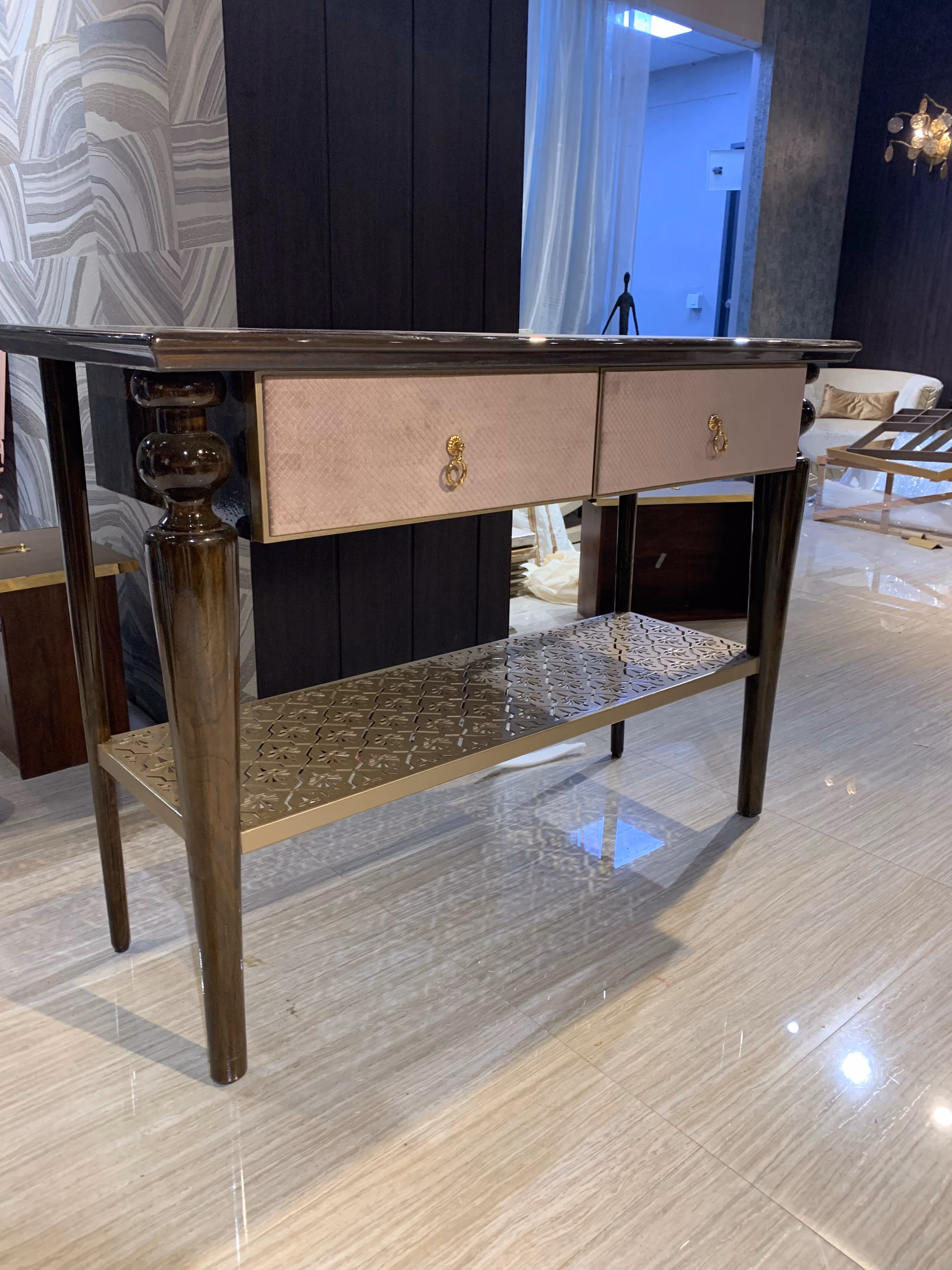 Console table with a dark glossy top, two blush quilted-velvet drawers with gold lion ring pulls, a pierced gold lower shelf and turned dark legs.