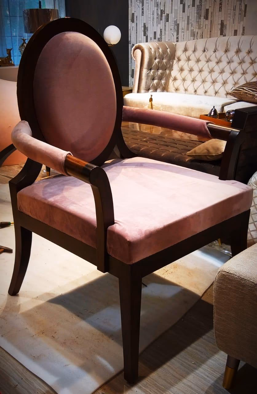 Dusty-rose velvet armchair with an oval medallion back, dark wood frame, wood-and-brass arm caps and tapered legs, in a styled showroom setting.