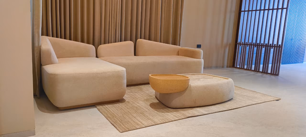 L-shaped oatmeal boucle sectional sofa with a low profile beside a rounded organic-shaped coffee table and sheer curtains.
