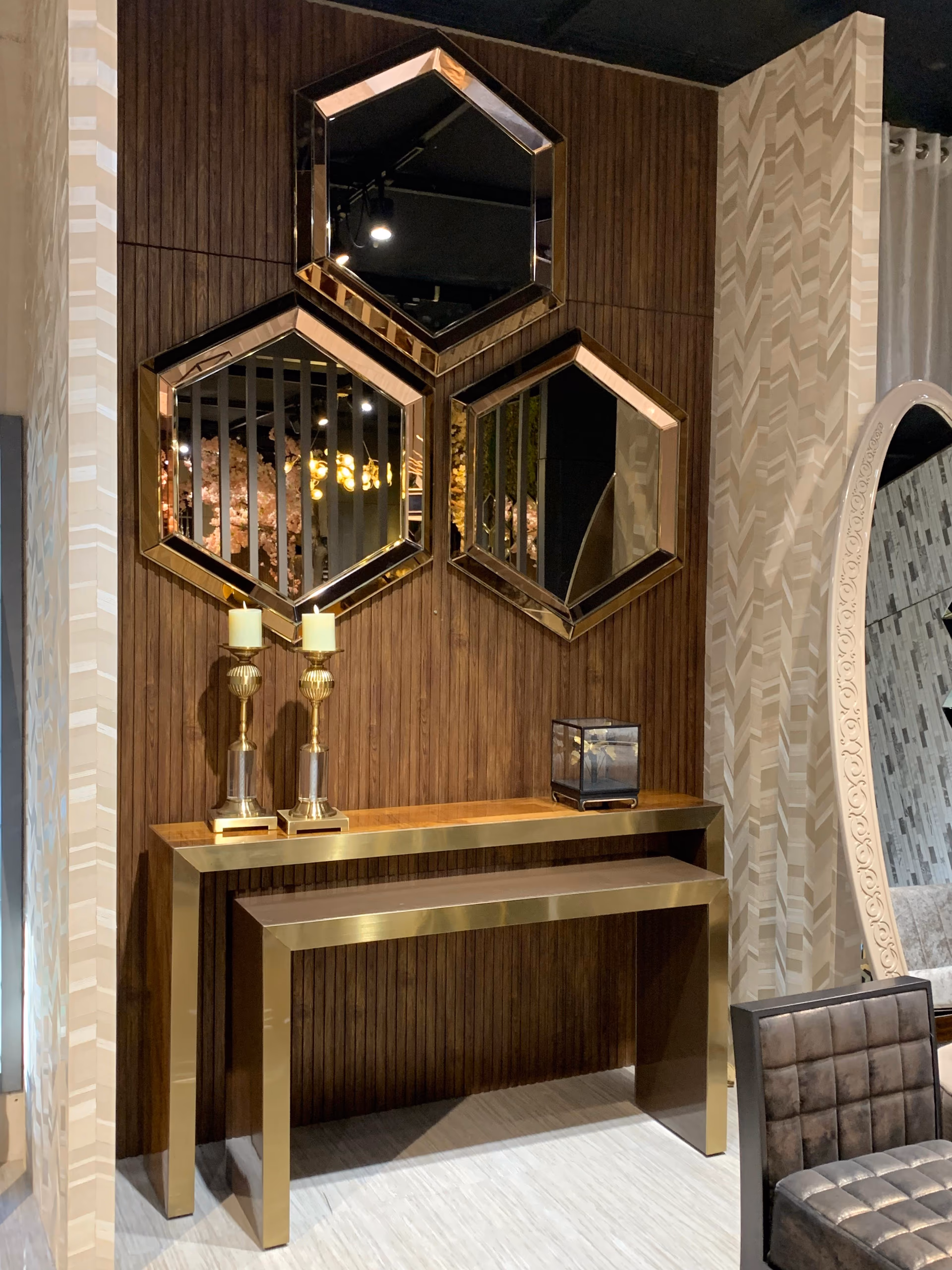 Slim brass-framed console with a wood top and a second smaller console nested beneath it, standing under three hexagonal rose-gold mirrors on a wood-slat wall.
