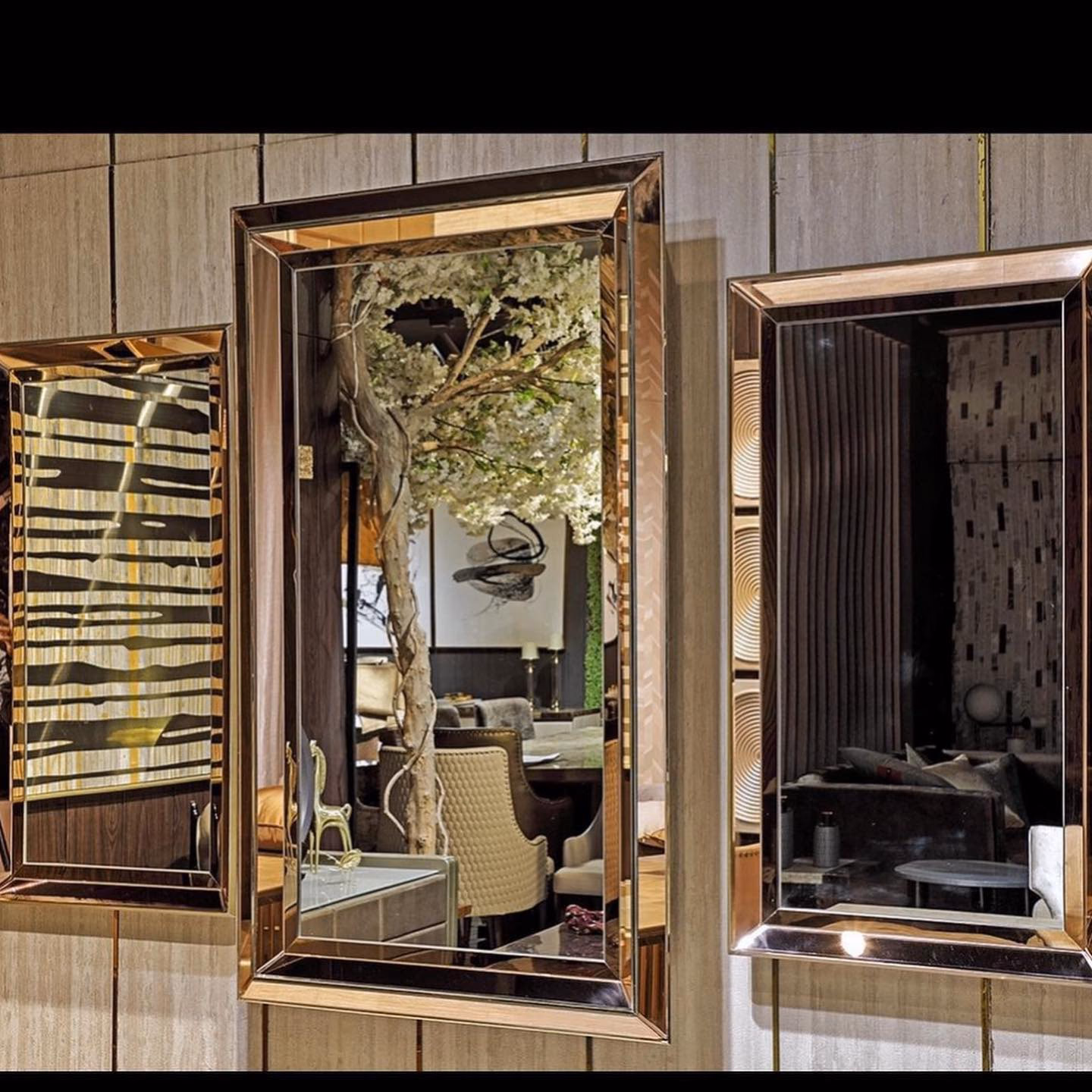 Set of three tall rectangular wall mirrors with wide bronze-tinted mirrored frames, each bevel cut and mitred at the corners, hung in a row on a travertine-clad wall.