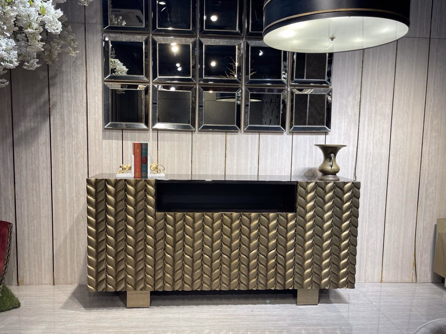 Long sideboard with doors carved into a deep bronze leaf and braid relief around a dark open centre shelf, shown beneath a grid of bevelled square wall mirrors.