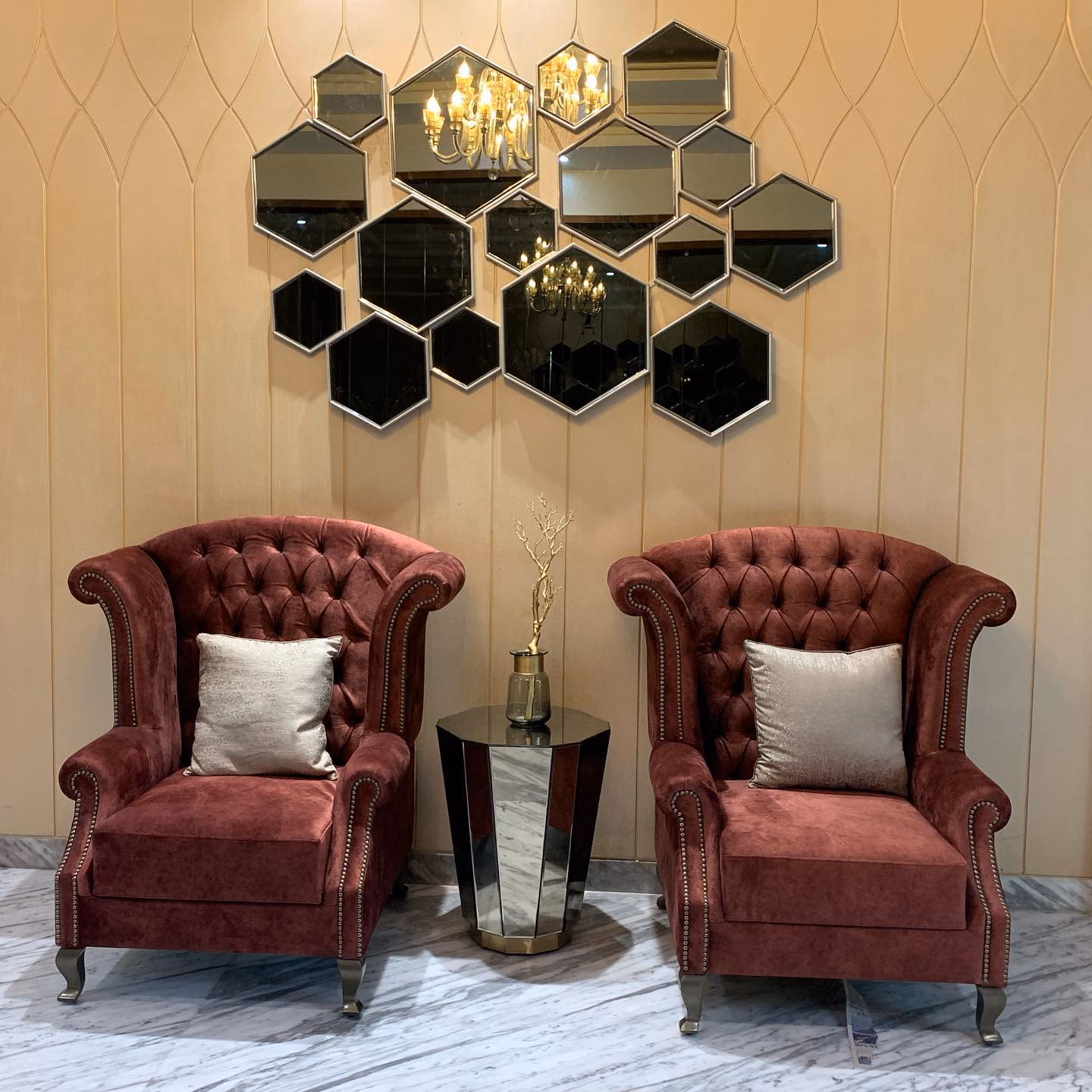 Pair of burgundy velvet chesterfield wingback armchairs with deep button tufting, antique nailhead trim along the arms and silvered cabriole legs, either side of a faceted mirrored side table.