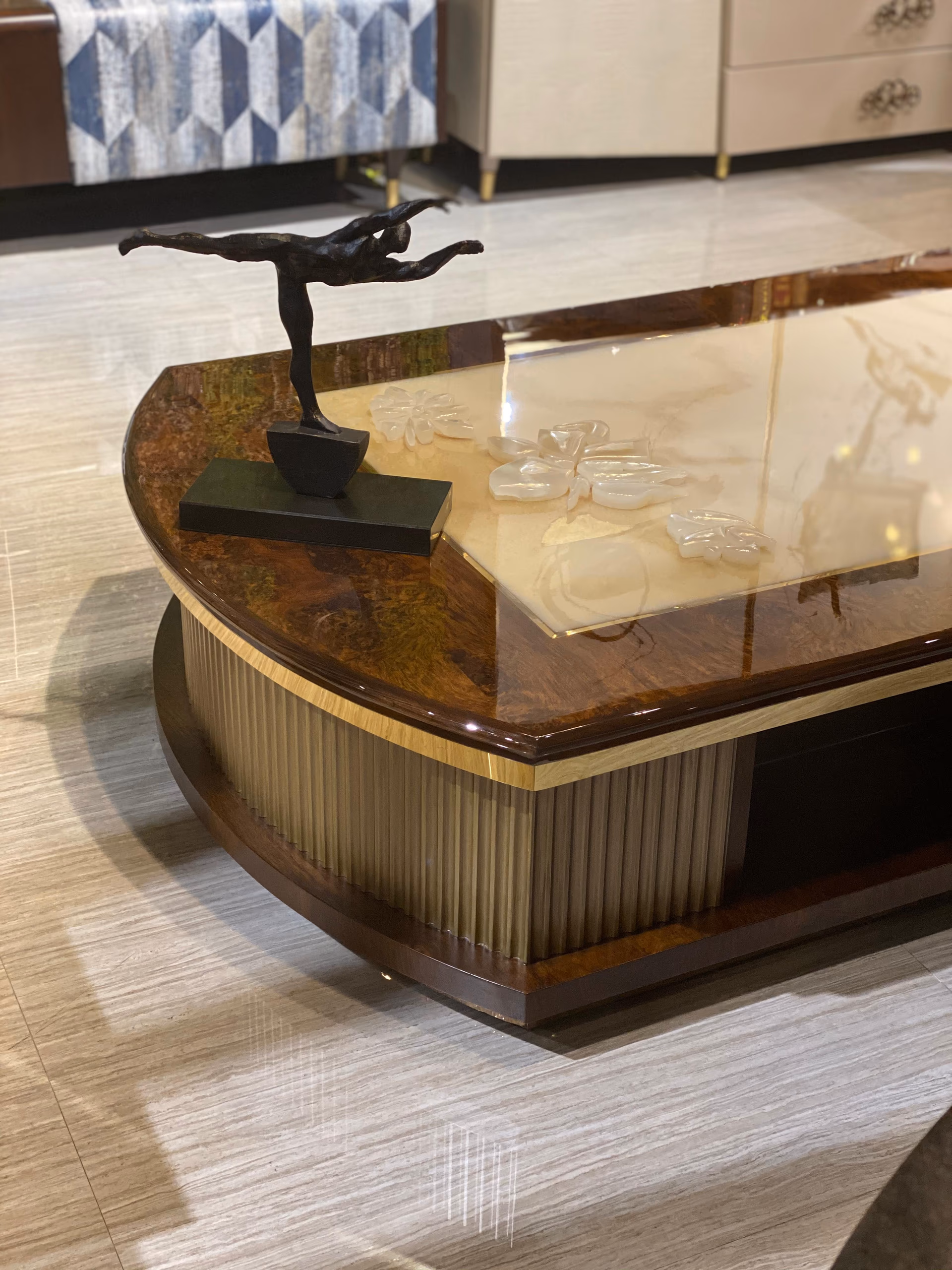 Corner of the coffee table where the glossy burl wood meets the carved onyx top, with a small bronze figure beside it.
