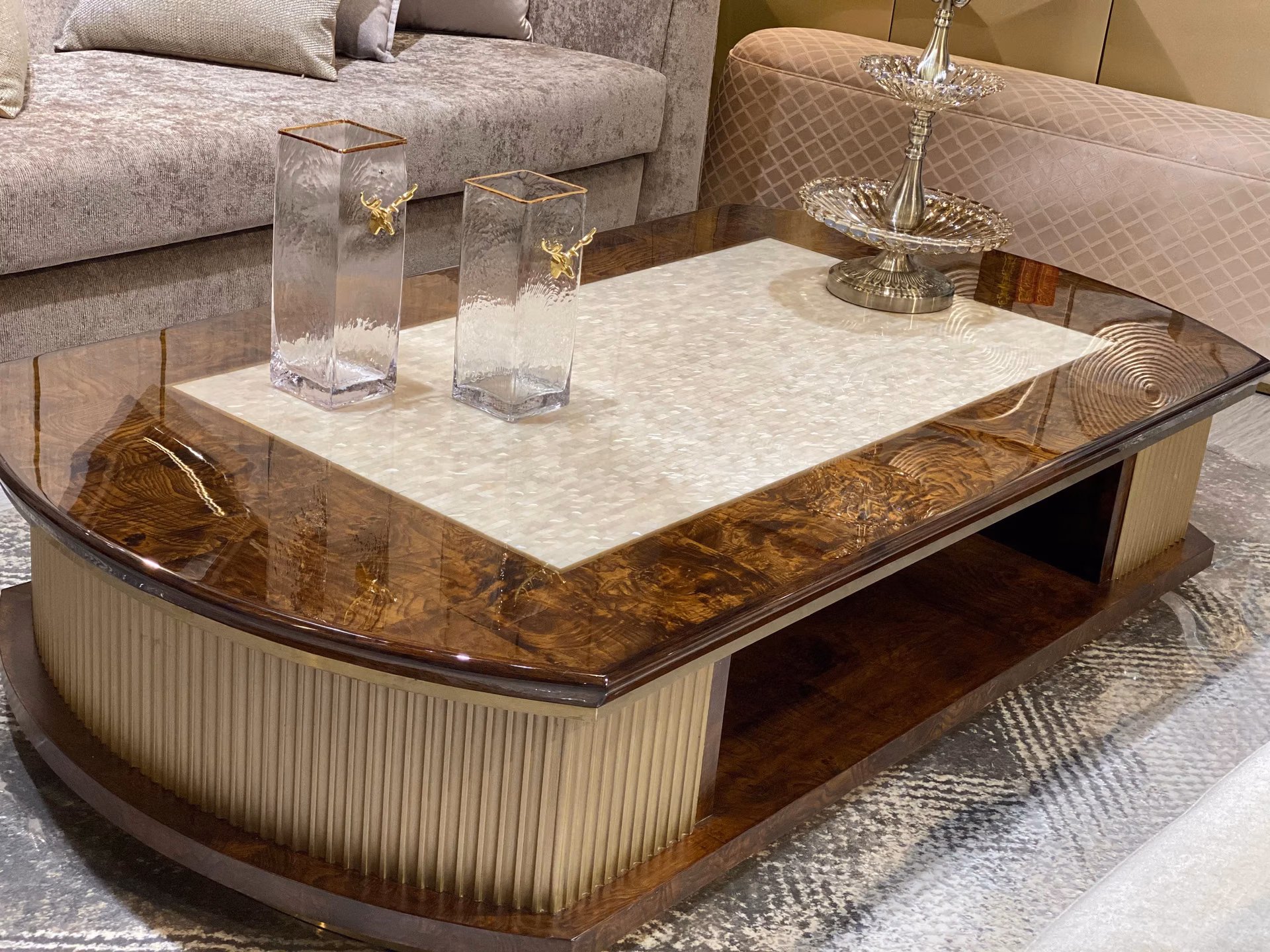 Round coffee table with a glossy burl-wood top set with pale mother-of-pearl inlay, raised on a fluted cream lacquer drum base on a marble floor.