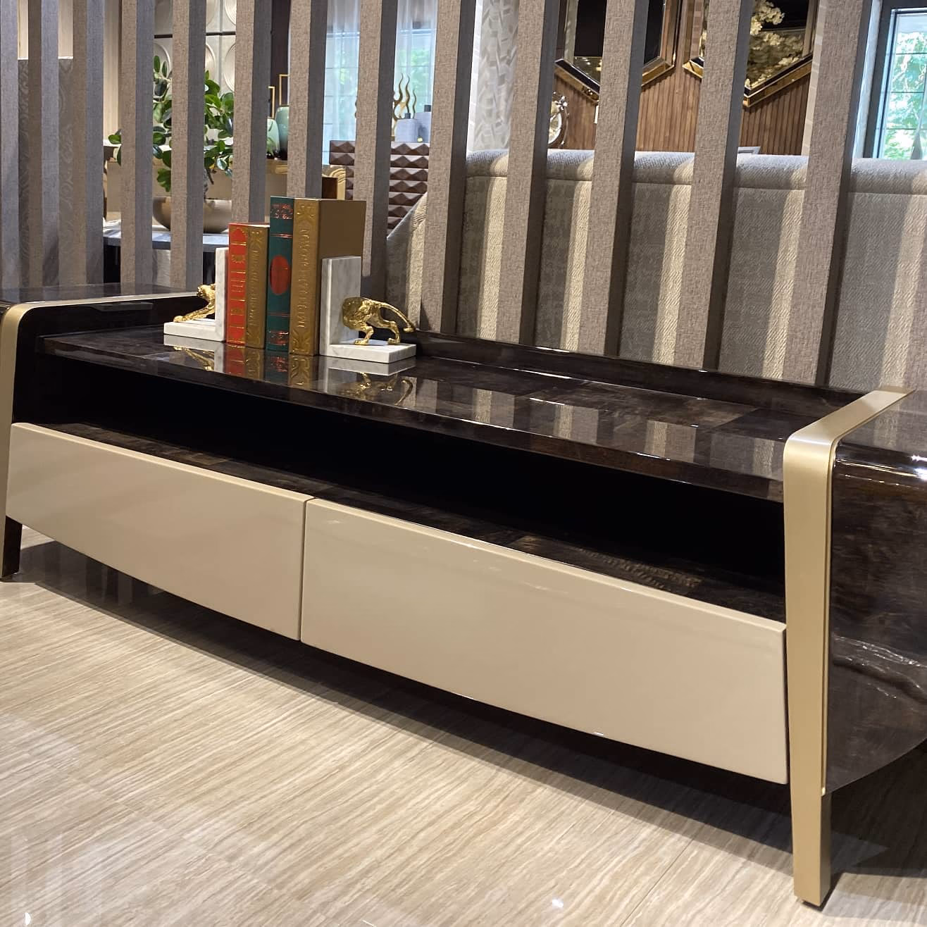 Low television unit with a dark burl-wood top, two wide ivory lacquer drawers, an open media gap and a champagne metal frame wrapping both ends.