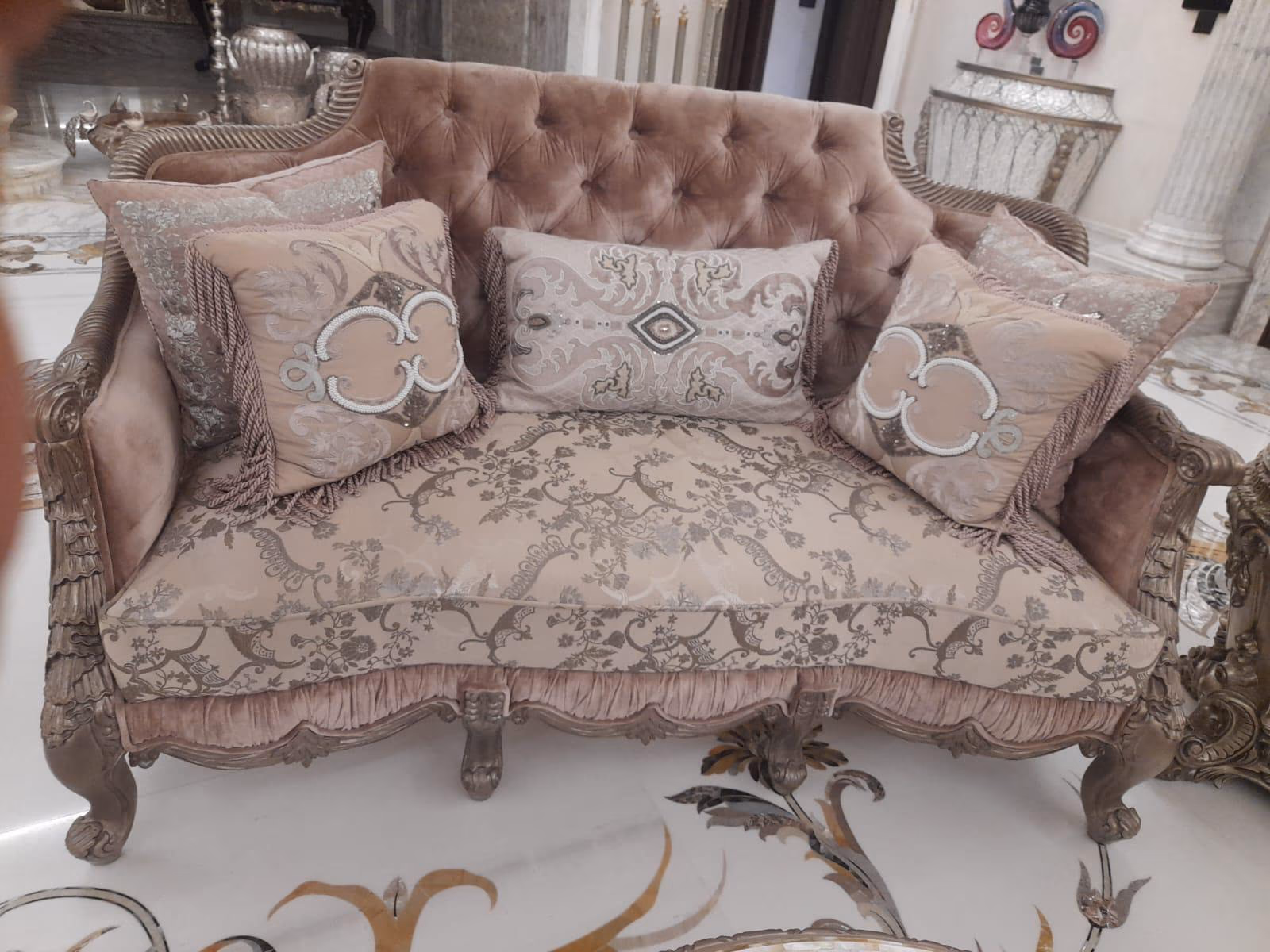 Two-seat blush sofa with a tufted velvet back, silver hand-carved frame, floral damask seat and carved claw feet, dressed with quatrefoil-motif cushions.