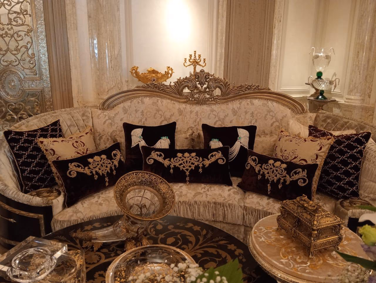 Cream damask three-seat sofa with a silver-carved rococo crown crest and dark embroidered cushions set behind a low black-and-gold inlay table.