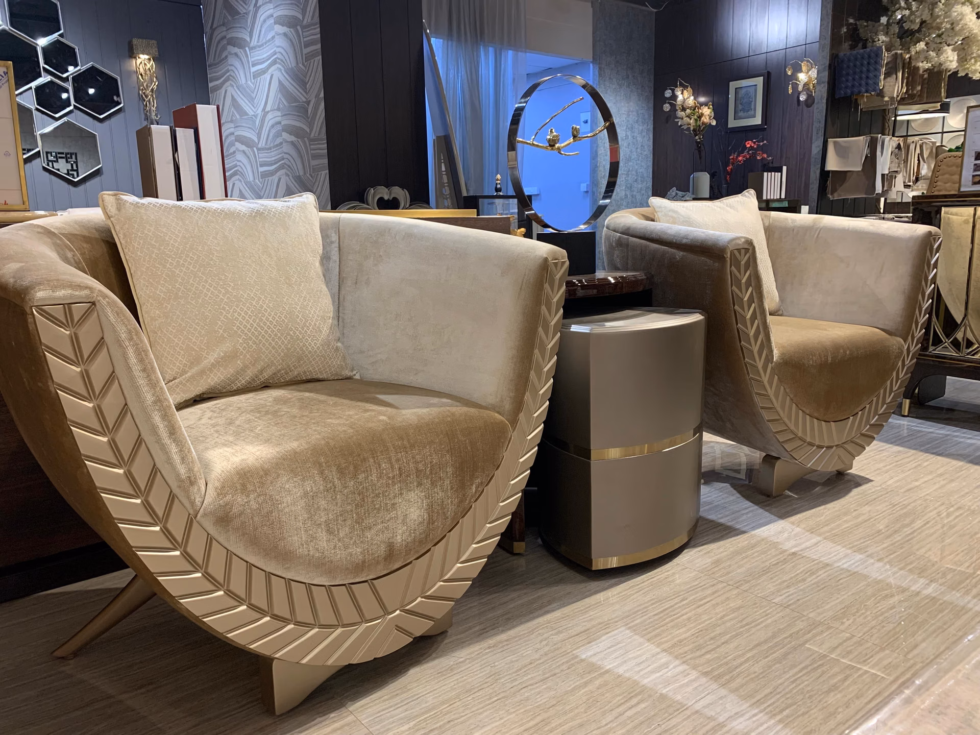 Pair of champagne velvet tub lounge chairs whose curved outer shells are carved with a leaf-vein chevron pattern, raised on splayed wood legs.