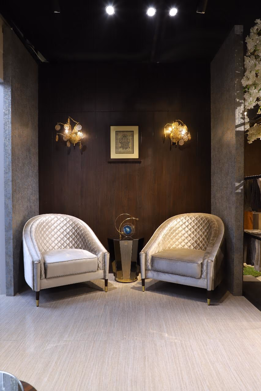 Pair of champagne velvet barrel chairs with diamond-quilted rounded backs and dark tapered legs with brass tips, flanking a small hexagonal side table.