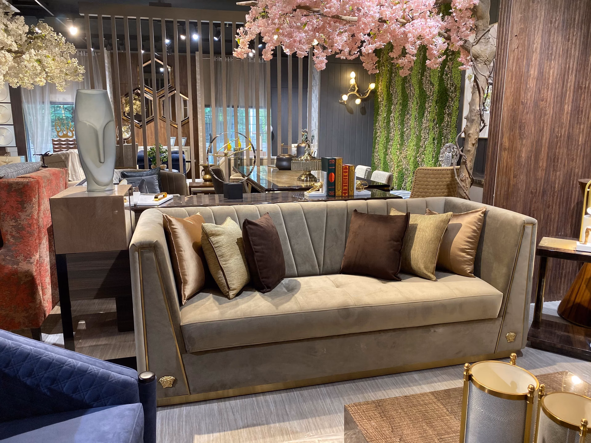 Three-seat sofa in champagne velvet with a curved channel-tufted back, loose seat cushions, a dark glossy wood base and small gold medallions at the corners.