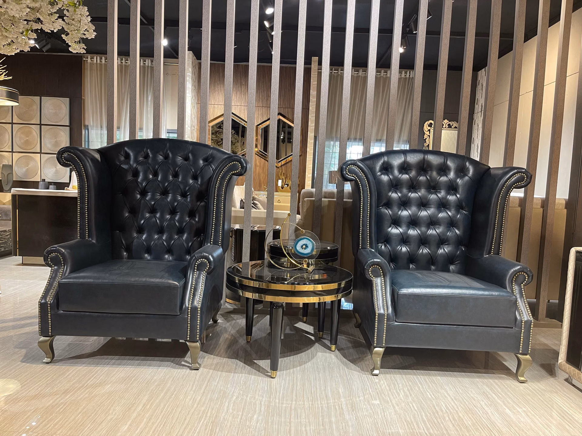 Pair of black leather chesterfield wingback chairs with deep tufting flanking a round drum table