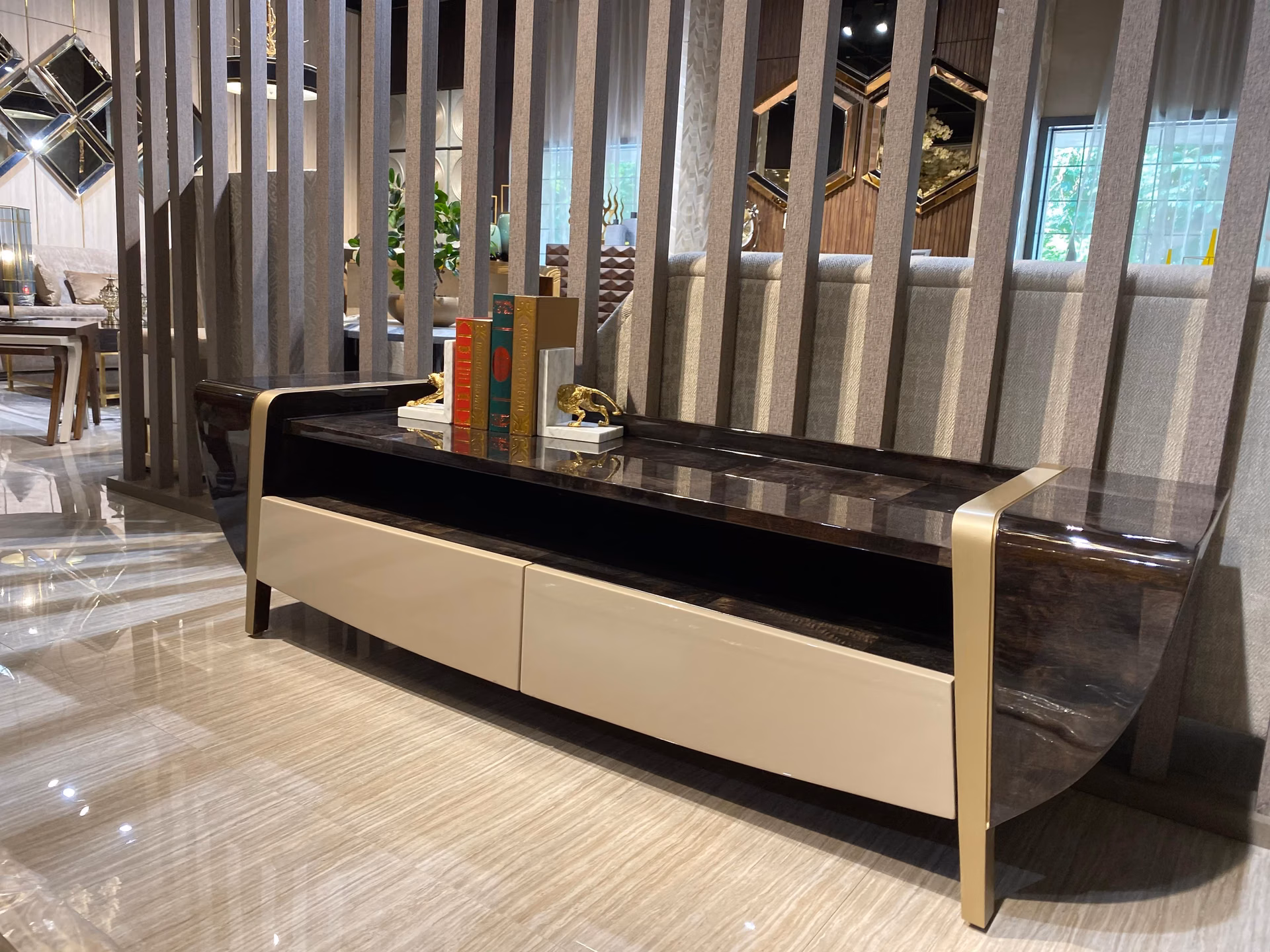 Long low console with a dark glossy stone top, two cream lacquer drawers and curved gold-trimmed waterfall legs, placed behind a sofa as a divider.