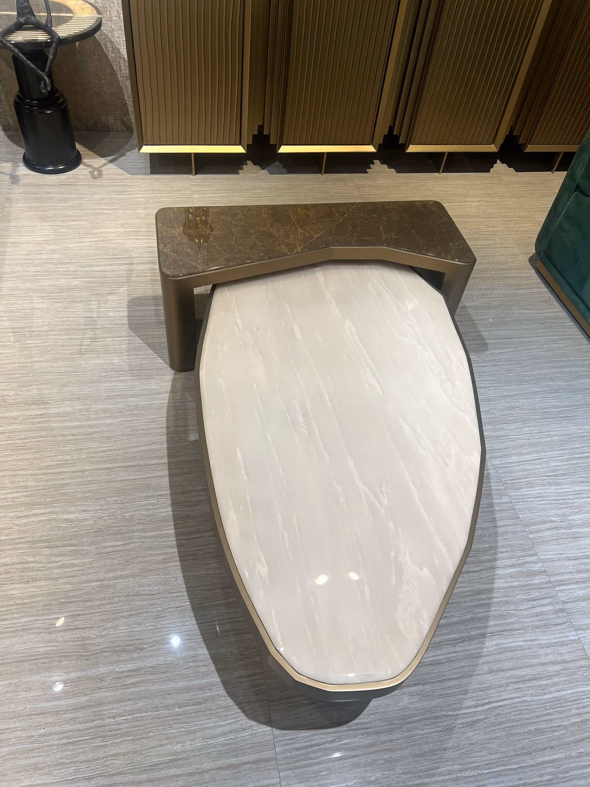 Two nesting coffee tables — one dark gold-veined marble on angled brass legs, one pale pink onyx oval on a gunmetal base.