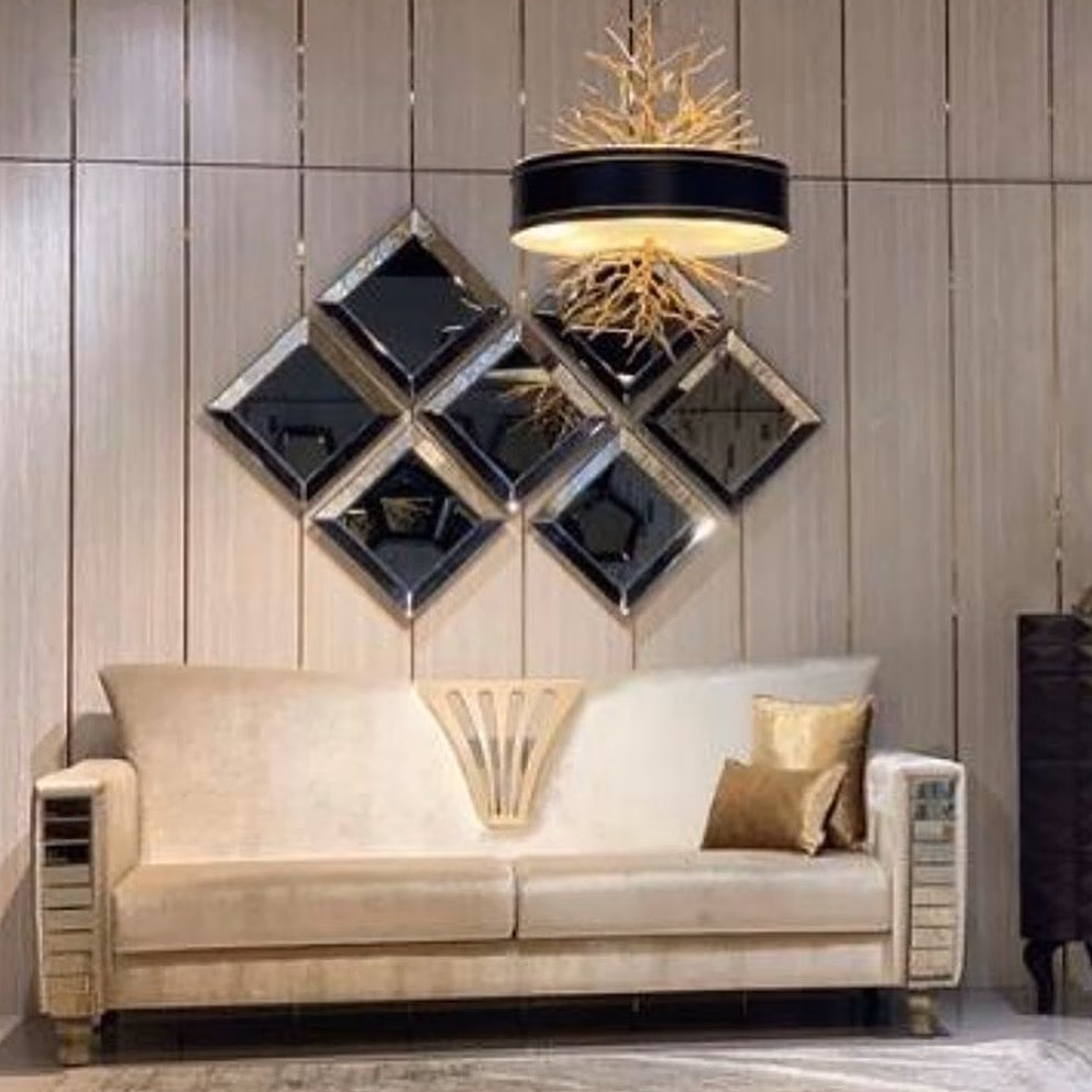 Wall cluster of seven diamond-shaped bevelled mirror panels in smoked and silver glass, arranged in a stepped grid above a cream velvet sofa with mirrored-strip arm panels.