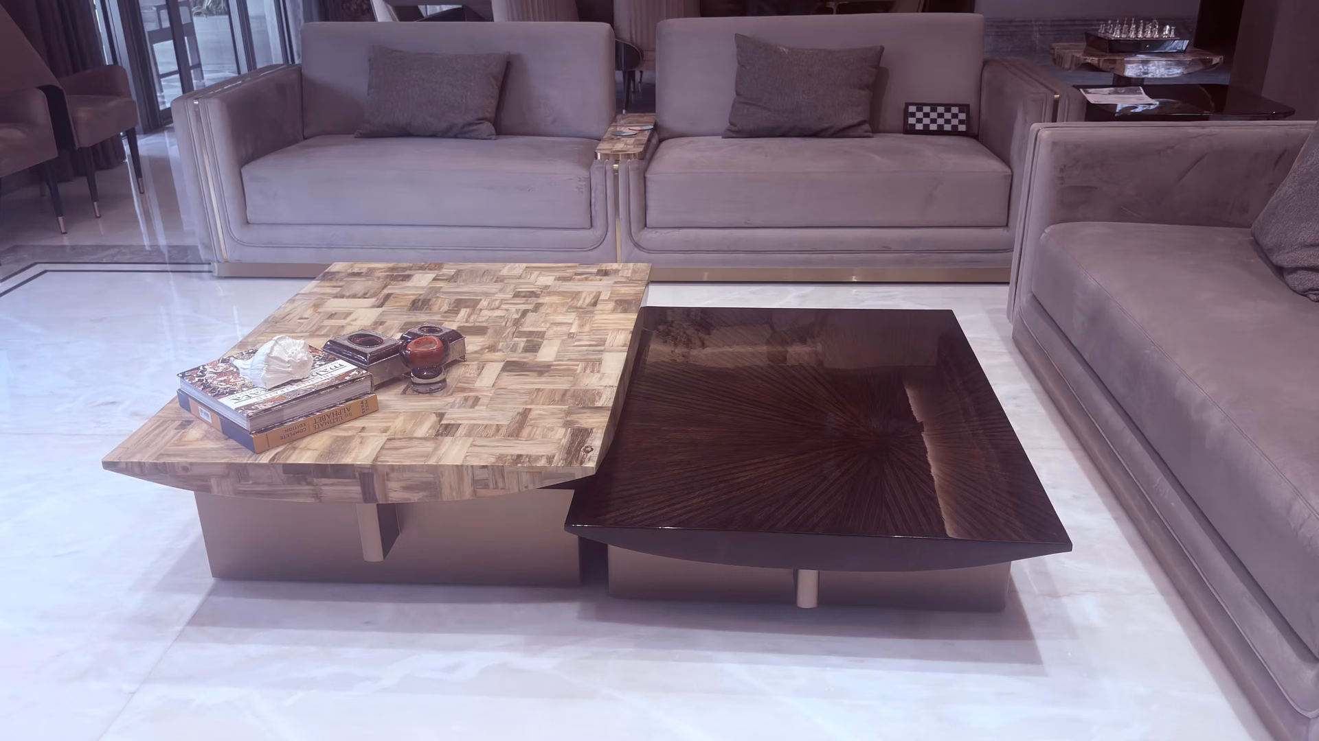 Two-piece low coffee table, one slab in honey petrified-stone mosaic and one in dark glossy sunburst wood, on brass bases over pale marble floor.