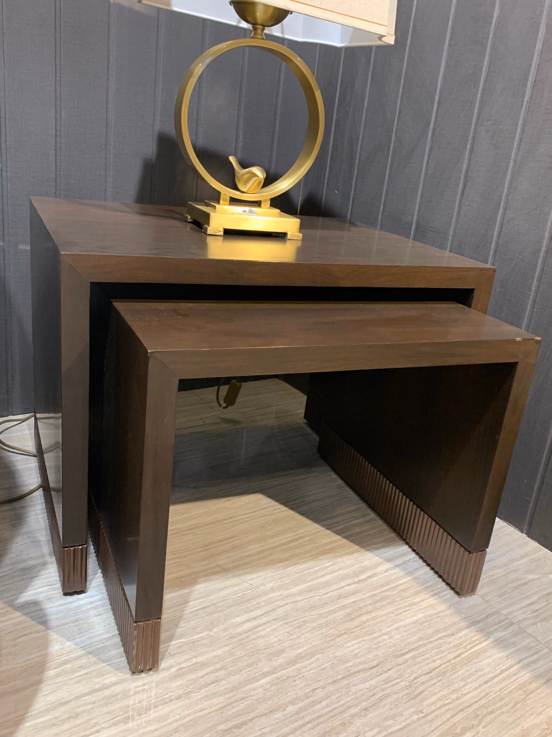 Pair of nesting side tables in dark walnut with waterfall sides and a fluted copper band around the base, topped by a brass ring table lamp.