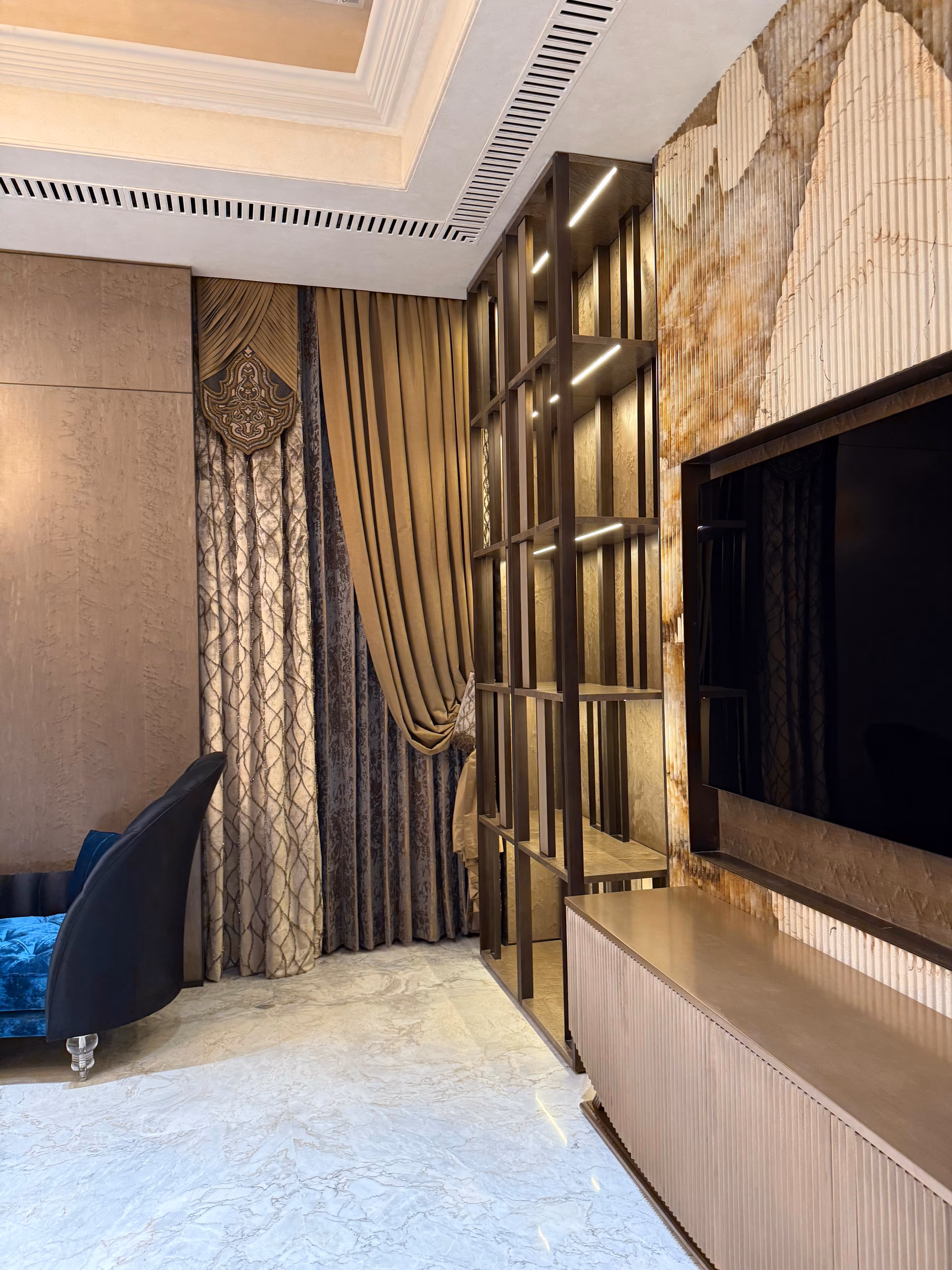 Fluted bronze-toned media console below a wall-mounted television, set against a backlit onyx panel and open shelving with brass edges.