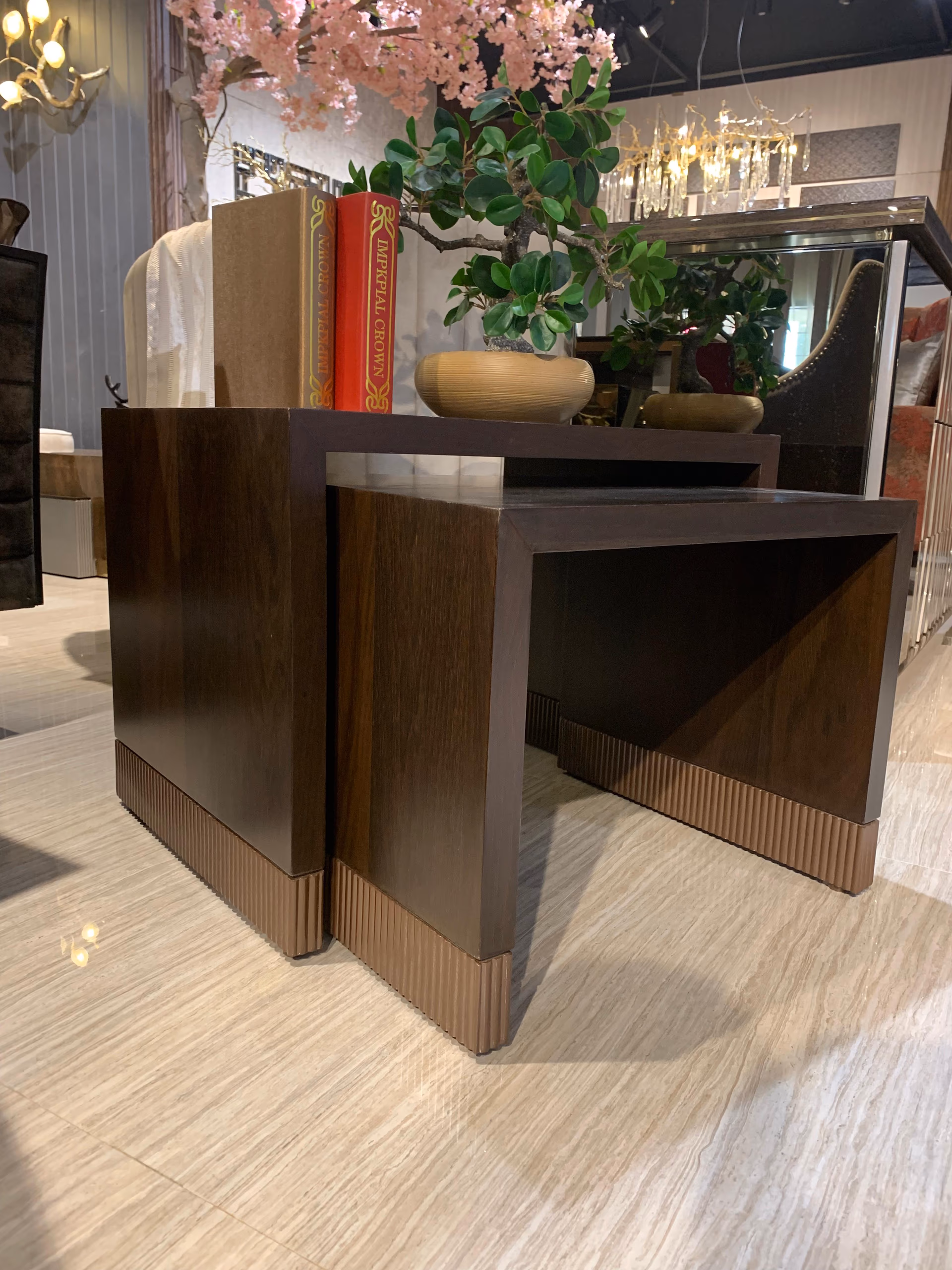 Angled view of the two dark walnut waterfall nesting tables with fluted copper bases, one pulled out from under the other, holding books and a bonsai.
