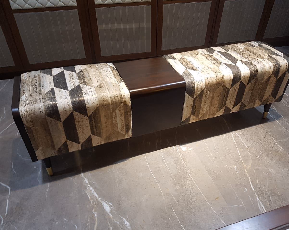 Long bench upholstered in a bold brown and cream geometric block print with a polished walnut centre panel dividing the two seats, on dark tapered legs with brass caps.
