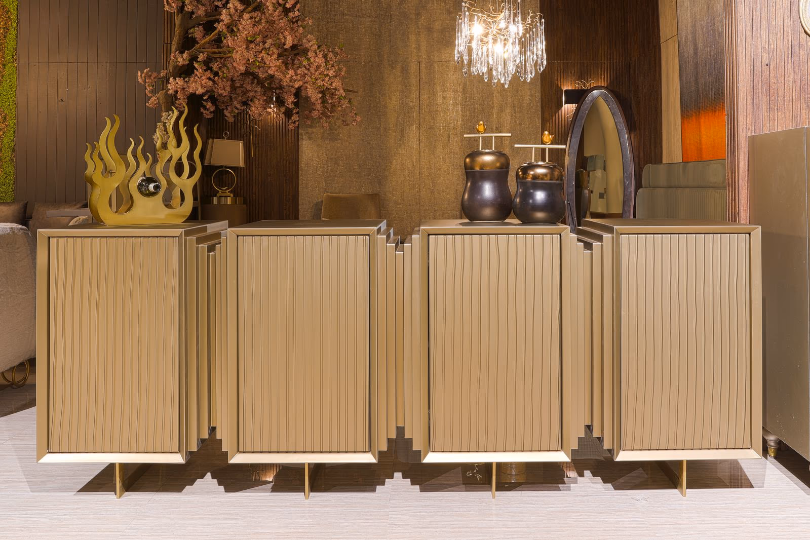 Long fluted gold cabinet with staggered zigzag door panels and slim brass legs, styled with jars and a sculpture on top.