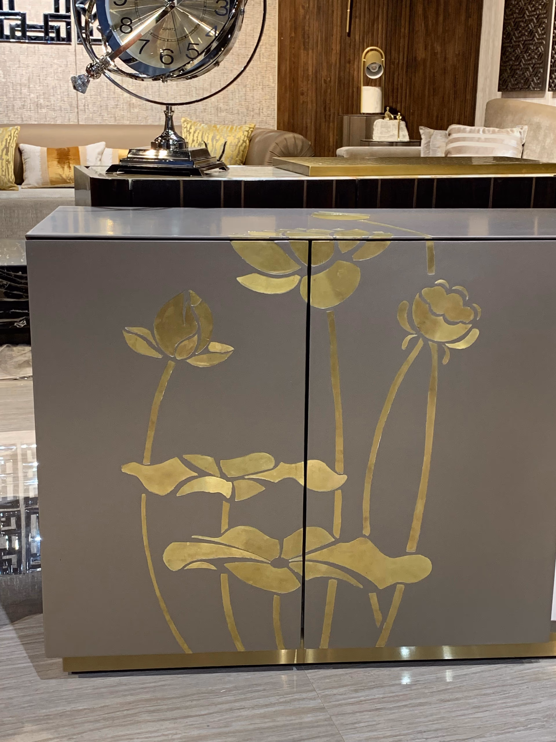 Two-door cabinet in soft grey lacquer with a hand-inlaid gold lotus-and-lily design climbing across both doors, on a slim brass base.