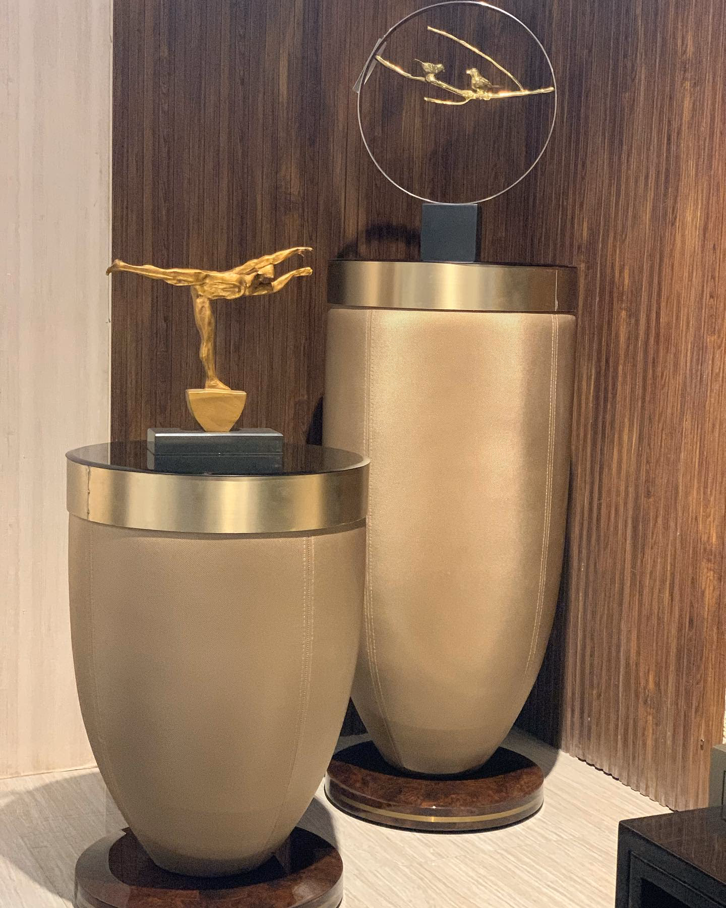 Pair of vase-shaped pedestal tables upholstered in soft gold suede with wide brushed brass collars, black glass tops and round burl-wood bases, in two heights.