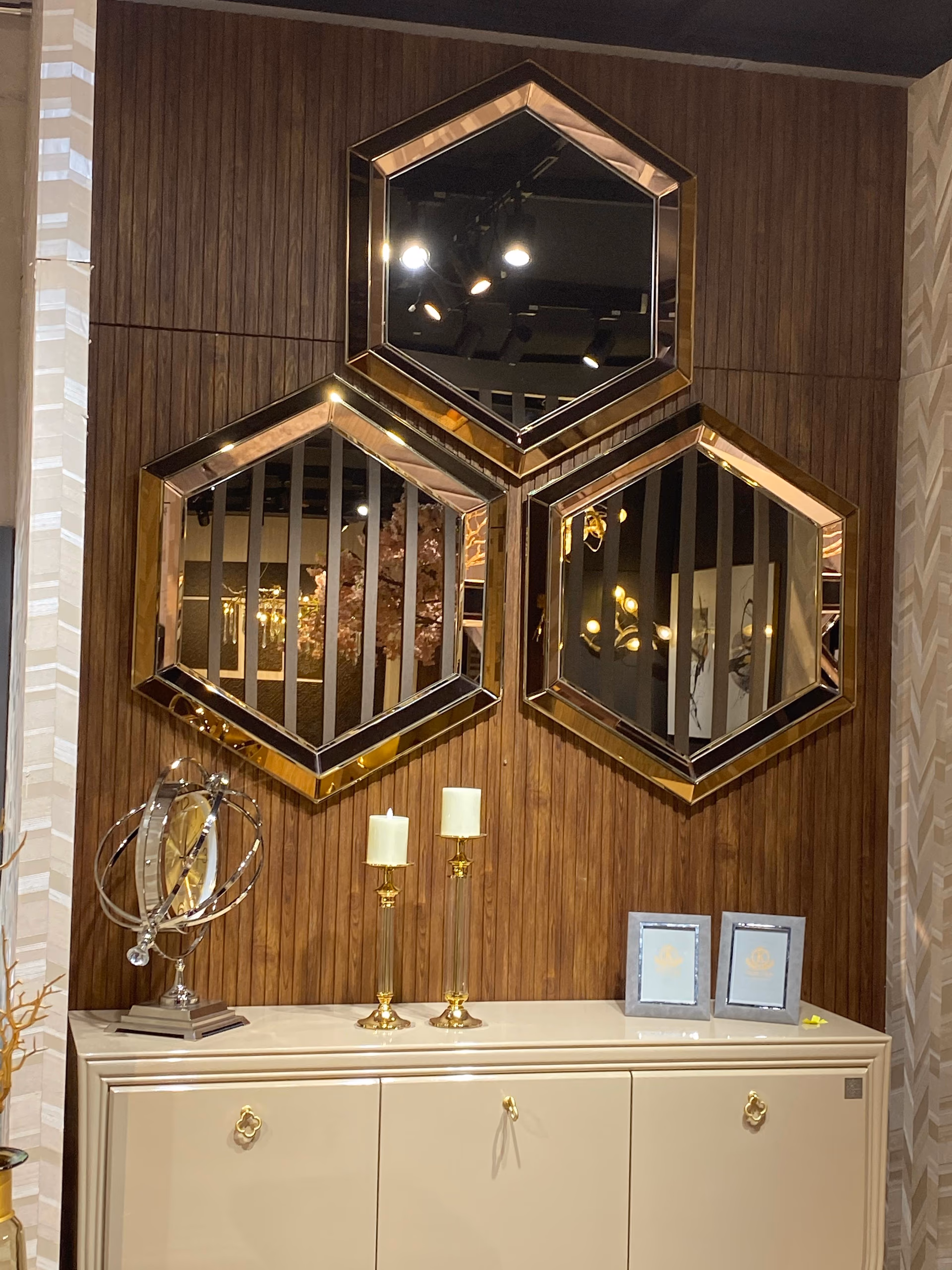 Three hexagonal wall mirrors with rose-gold and black bevelled frames, arranged in a honeycomb above a cream cabinet with gold quatrefoil knobs.