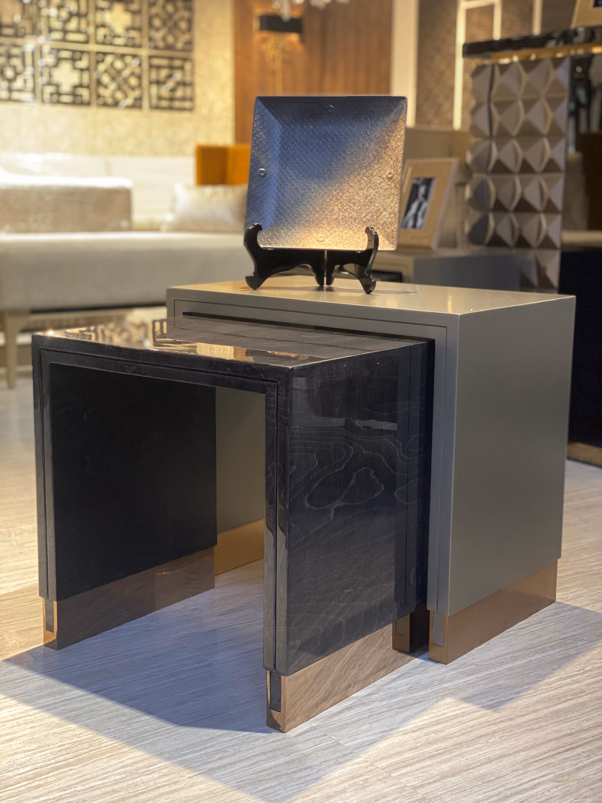 Nesting side table set with a taupe lacquer cube table and a smaller glossy black wood-grain table tucked beneath it, both on slim brass toe caps.