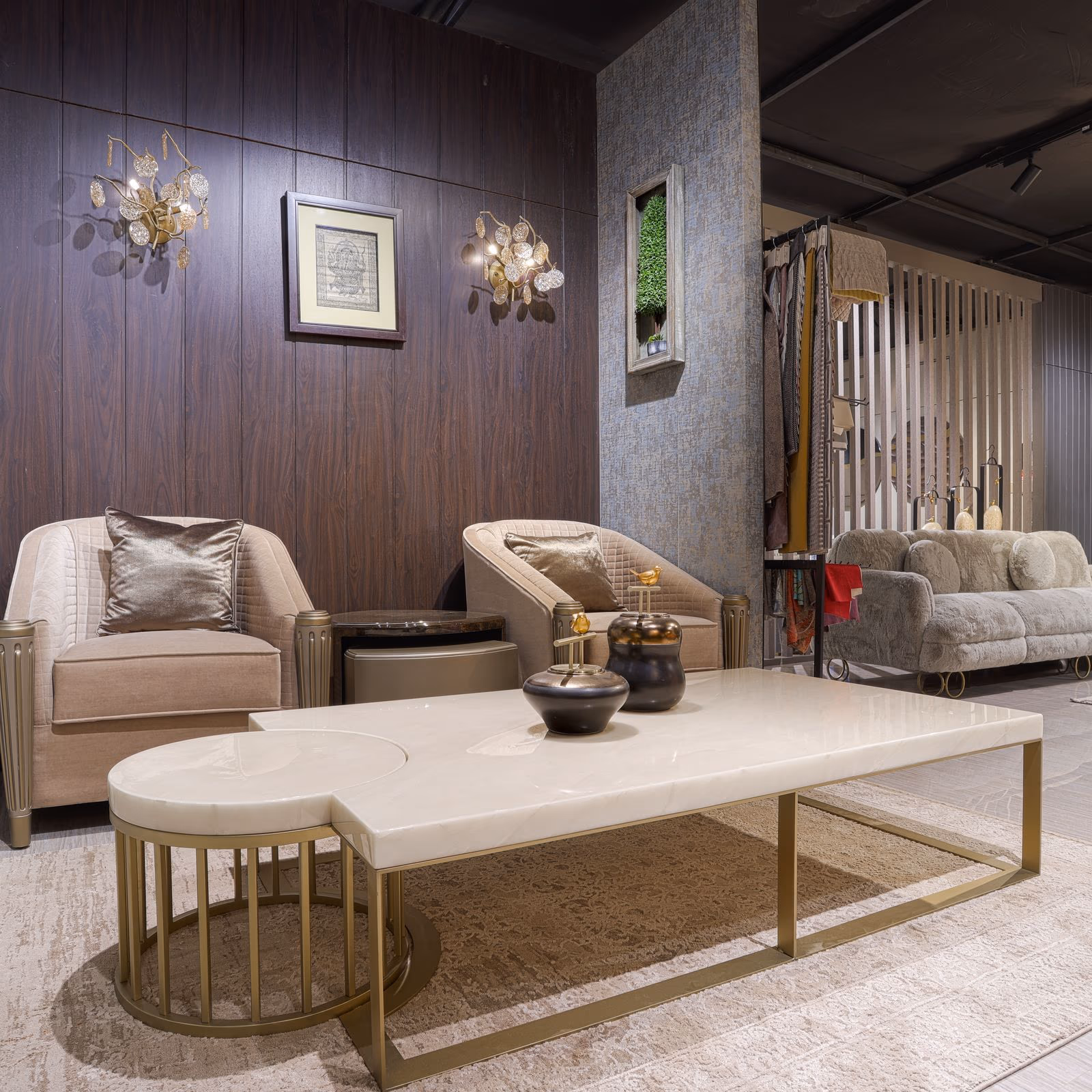 Living room grouping of a round-and-rectangular white marble coffee table on a brass frame flanked by two taupe quilted armchairs.
