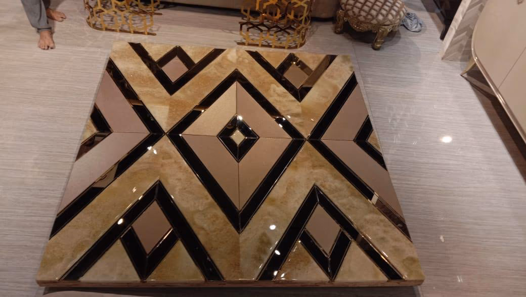 Top-down view of a square coffee table inlaid with a bold chevron pattern of bronze mirror, black glass and honey onyx forming a central diamond.