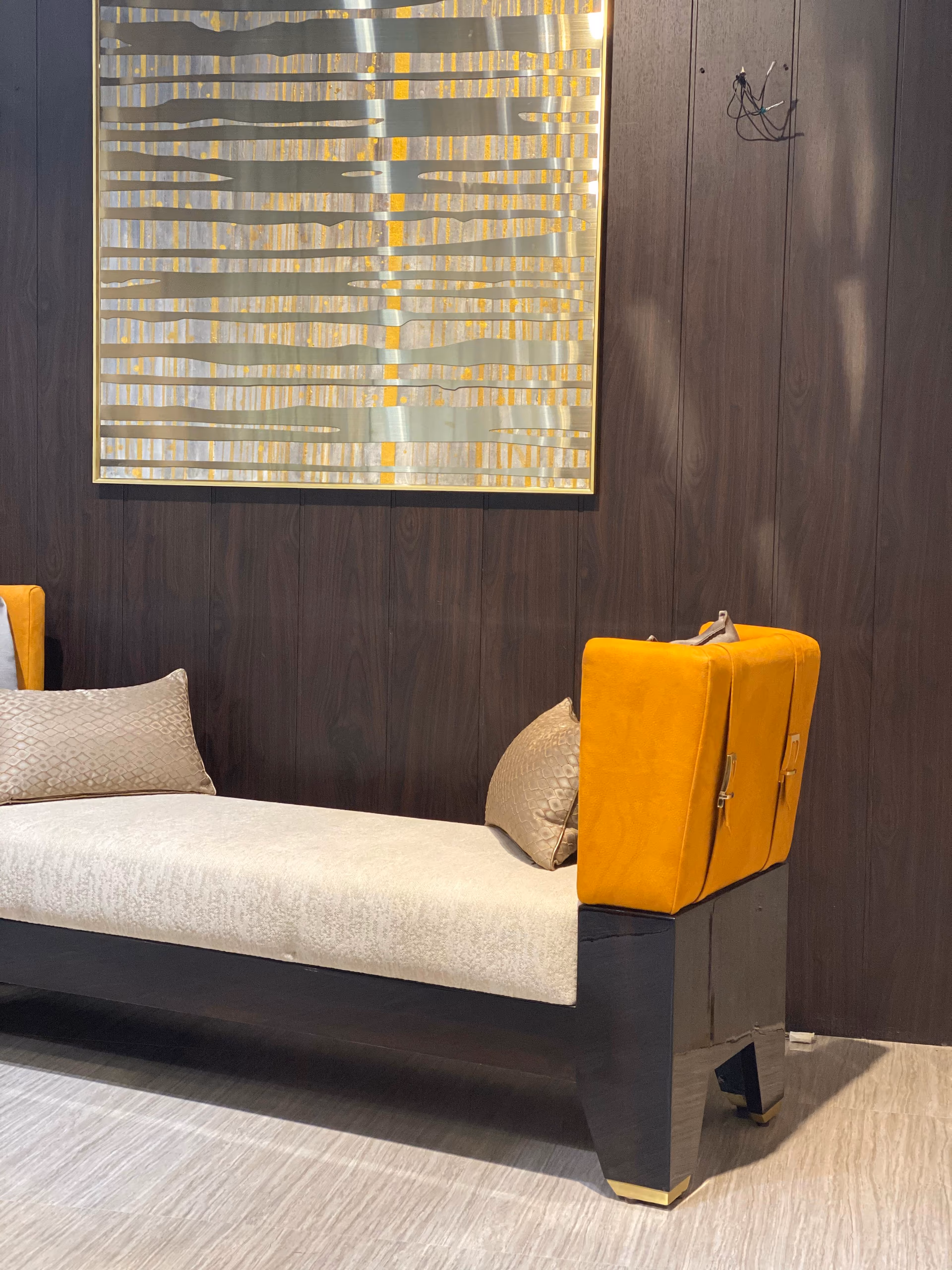 Close look at one end of the daybed, showing the mustard velvet bolster, its buckle strap and the brass-capped wooden leg.