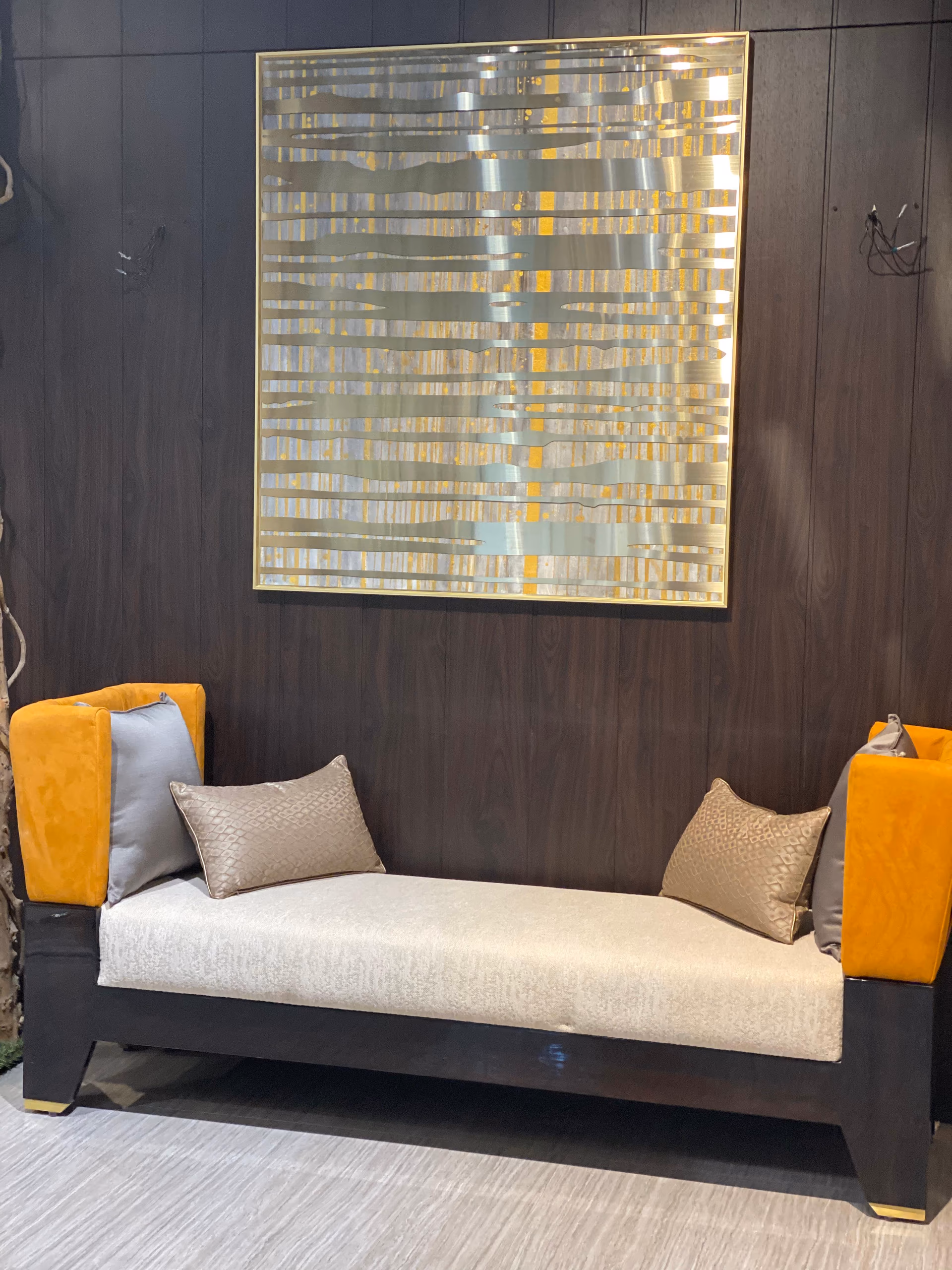 Backless daybed with a cream seat cushion and two upright mustard velvet bolster ends held by buckle straps, on a dark wood frame with brass feet.