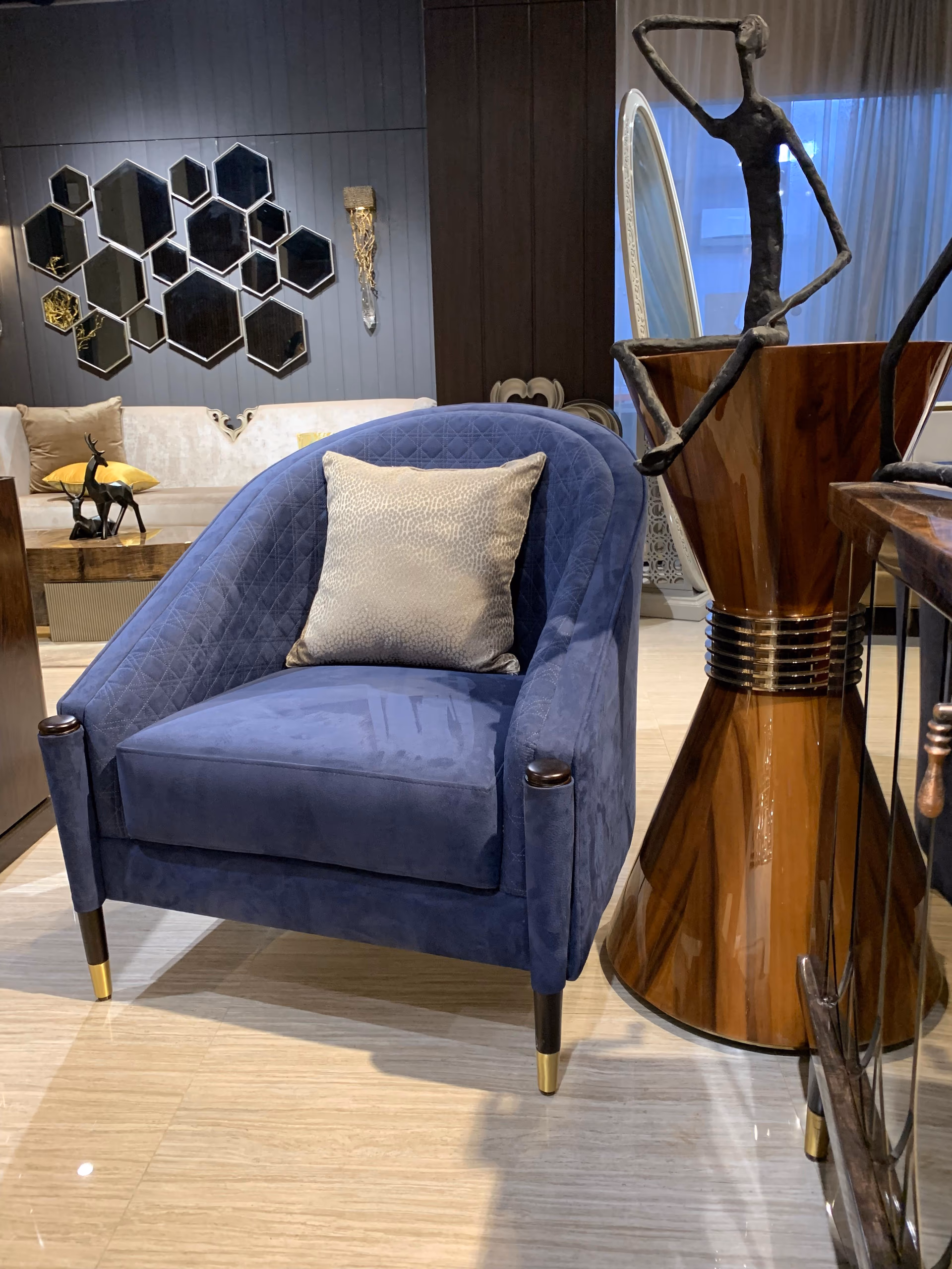 Navy blue velvet barrel accent chair with a curved diamond-quilted back and a soft cushion, standing on brass-capped dark wood legs.