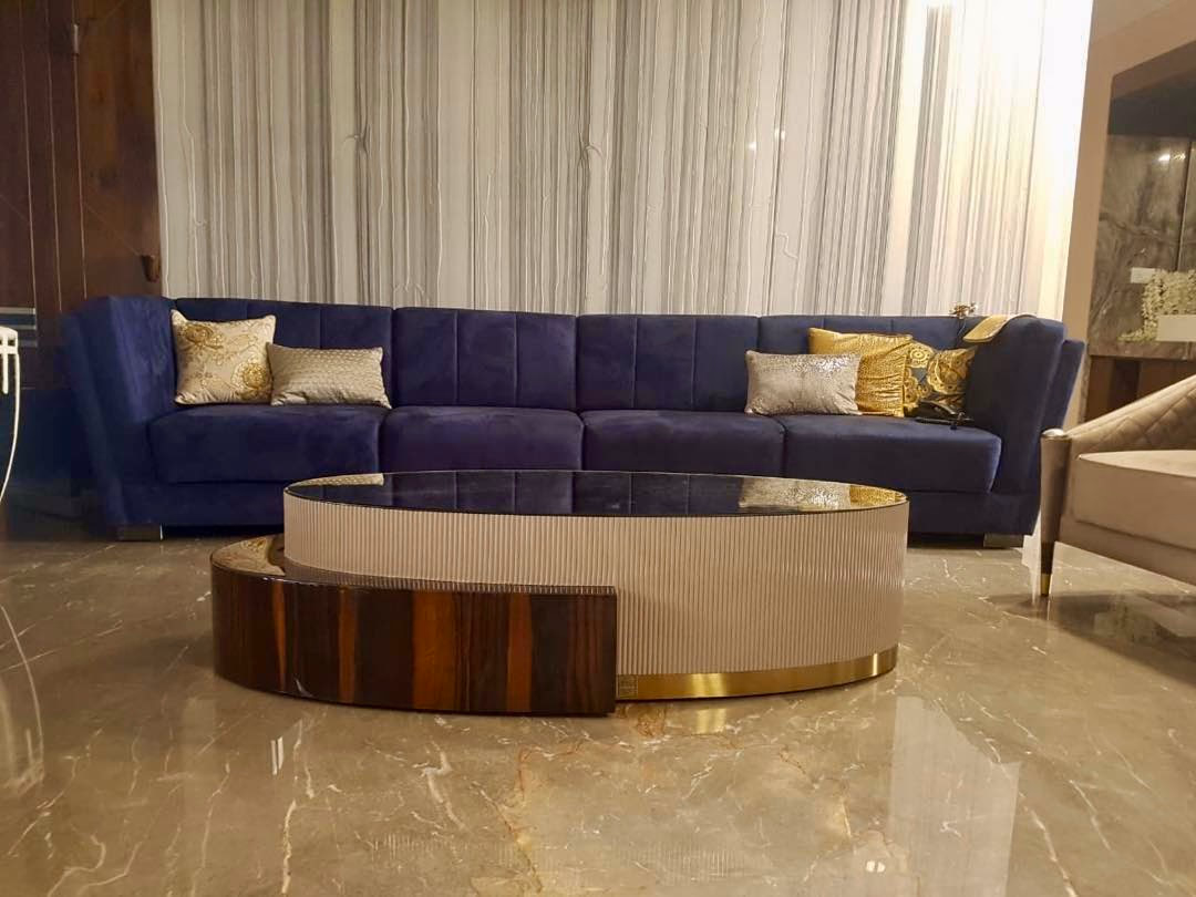 Long navy velvet sectional with vertical channel cushioning and a corner return, paired with a two-tier oval coffee table in fluted ivory lacquer and glossy rosewood on a brass plinth.