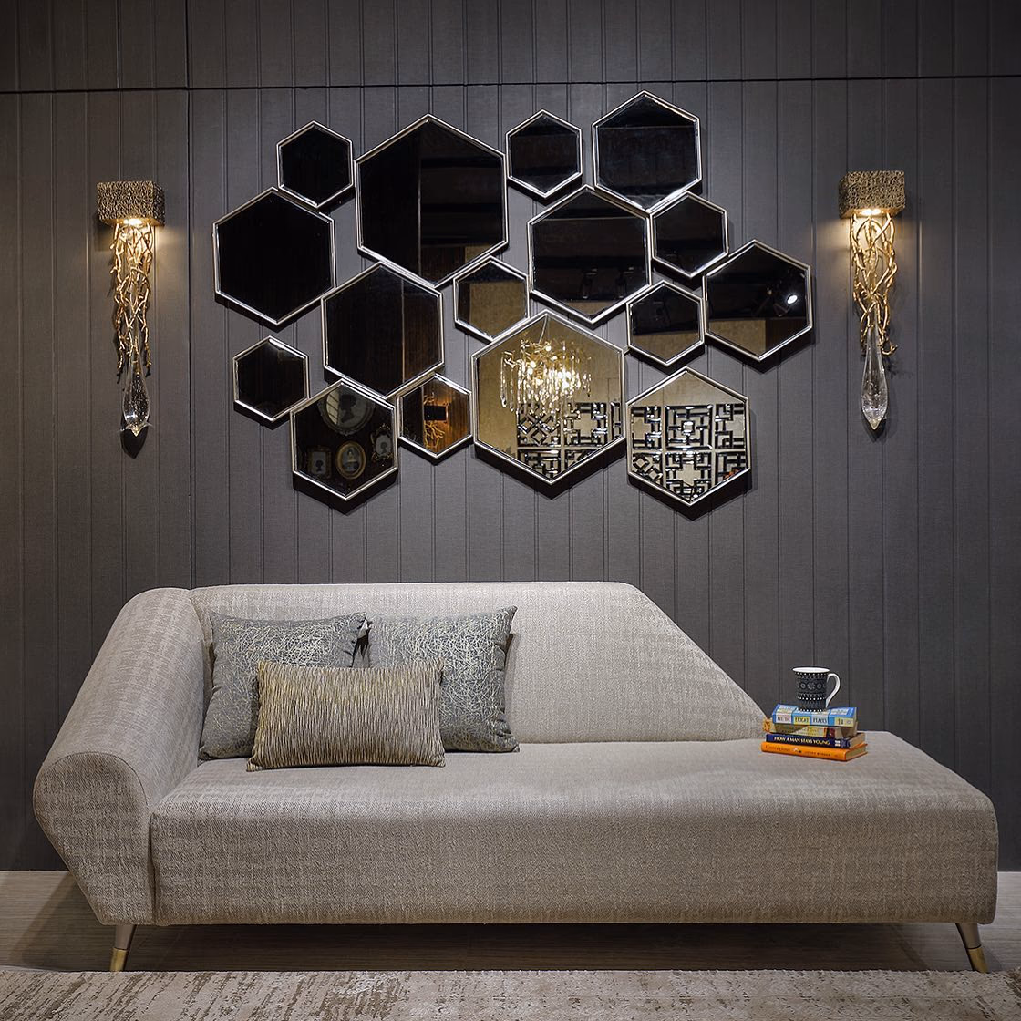 Low armless chaise daybed in textured oatmeal linen with a single rolled bolster end and a long flat seat, standing on slim splayed brass legs beneath a hexagonal mirror cluster.