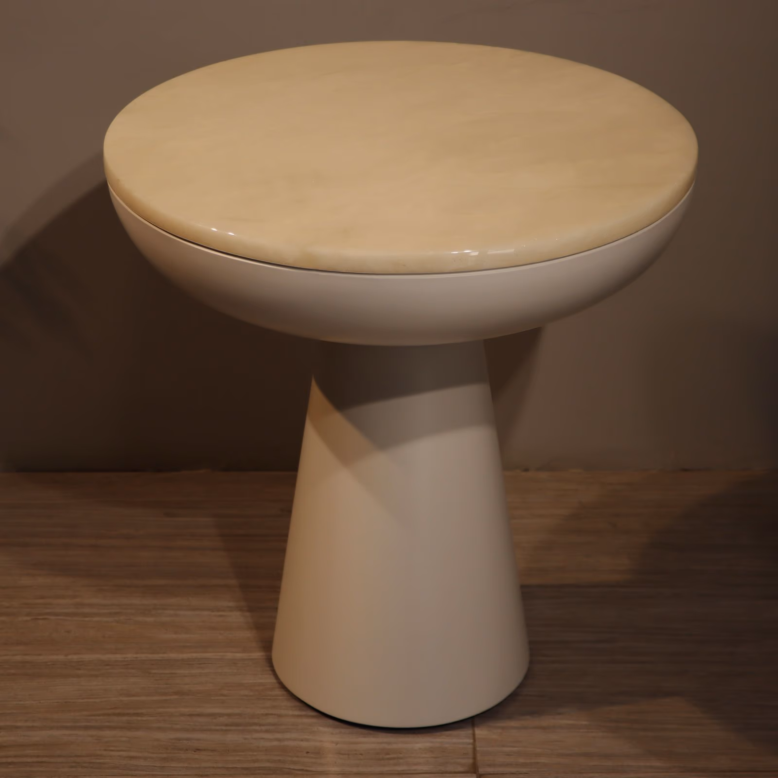 Round honey-toned onyx tabletop resting in a glossy cream bowl-shaped base on a tapering cone pedestal.