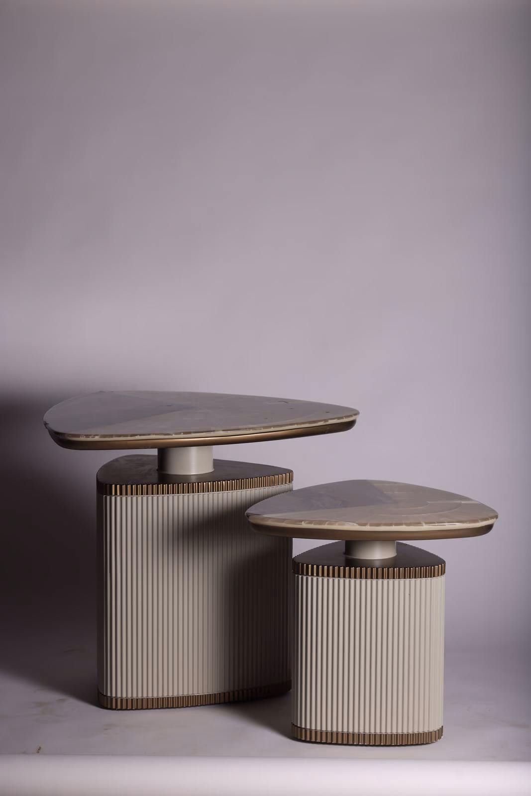 Two organic pebble-shaped marble-top tables of different heights on ribbed bronze-trimmed cylinder bases.