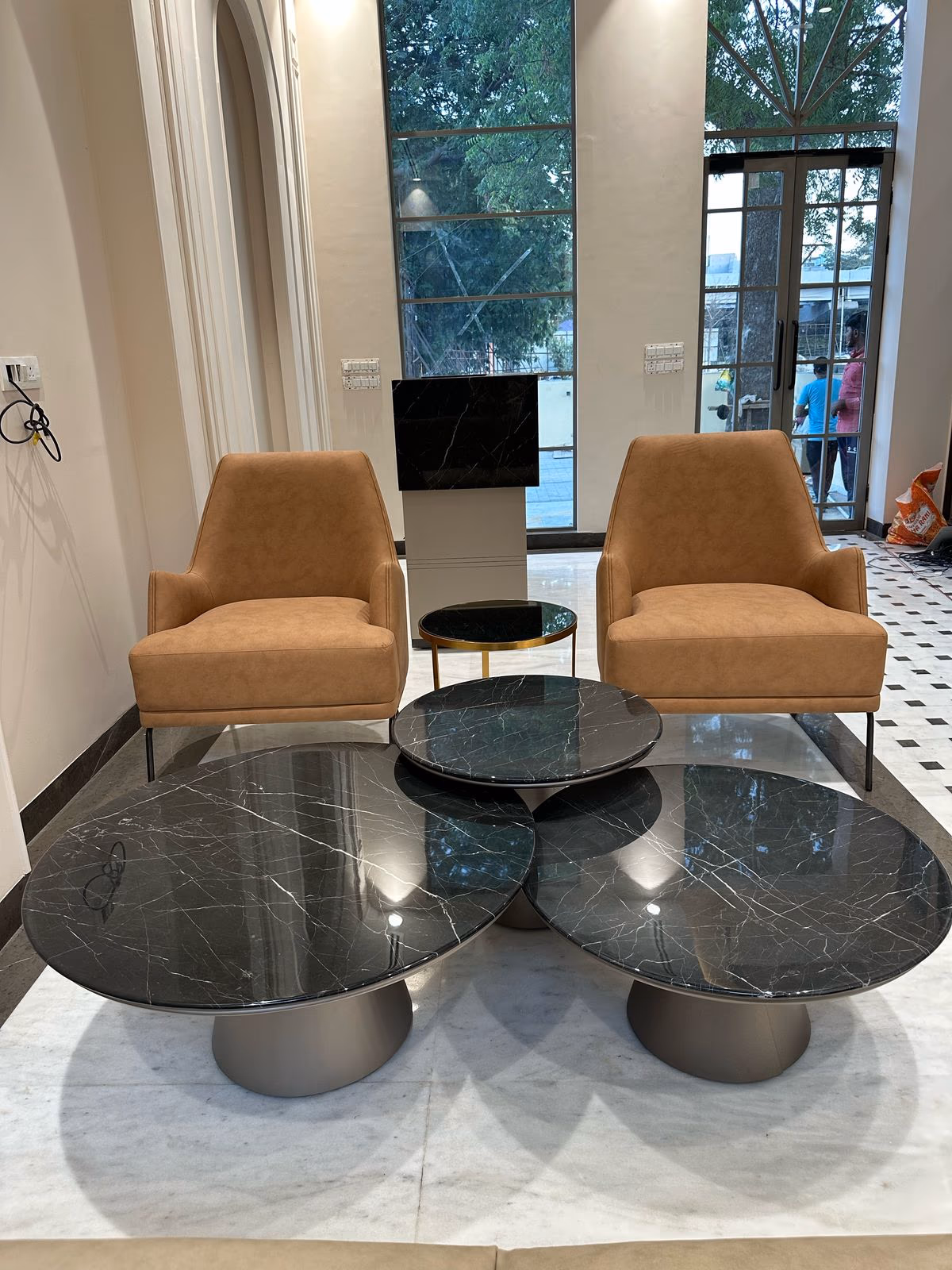 Three round black marble-top coffee tables on grey pedestal bases clustered together in front of a pair of cognac leather chairs.