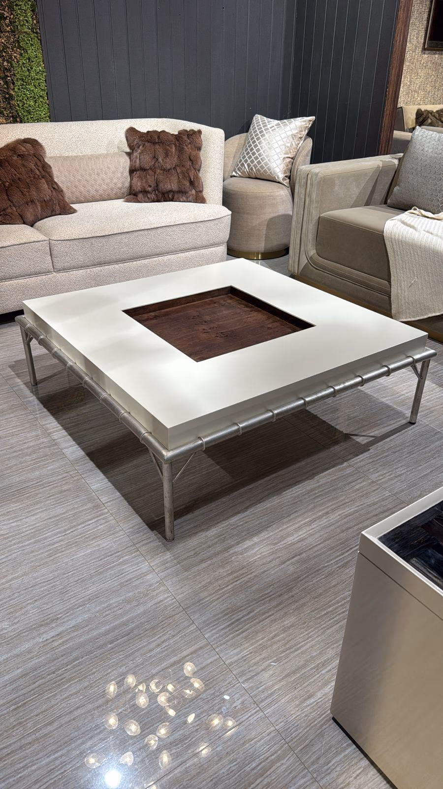 Large square coffee table with a cream lacquer top framing a dark burl-wood inset centre, raised on a slim silver faux-bamboo metal frame, on grey tile.