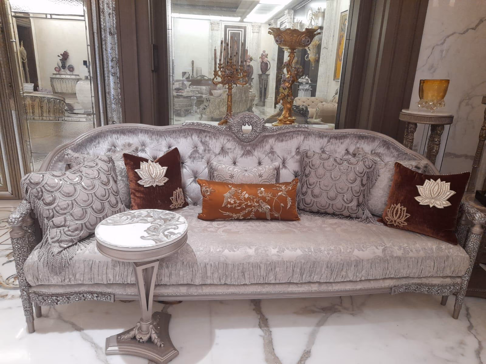Silver-grey three-seat sofa with a button-tufted velvet back, rose-cluster carved crest, damask seat and mixed fish-scale, lotus and bird cushions.